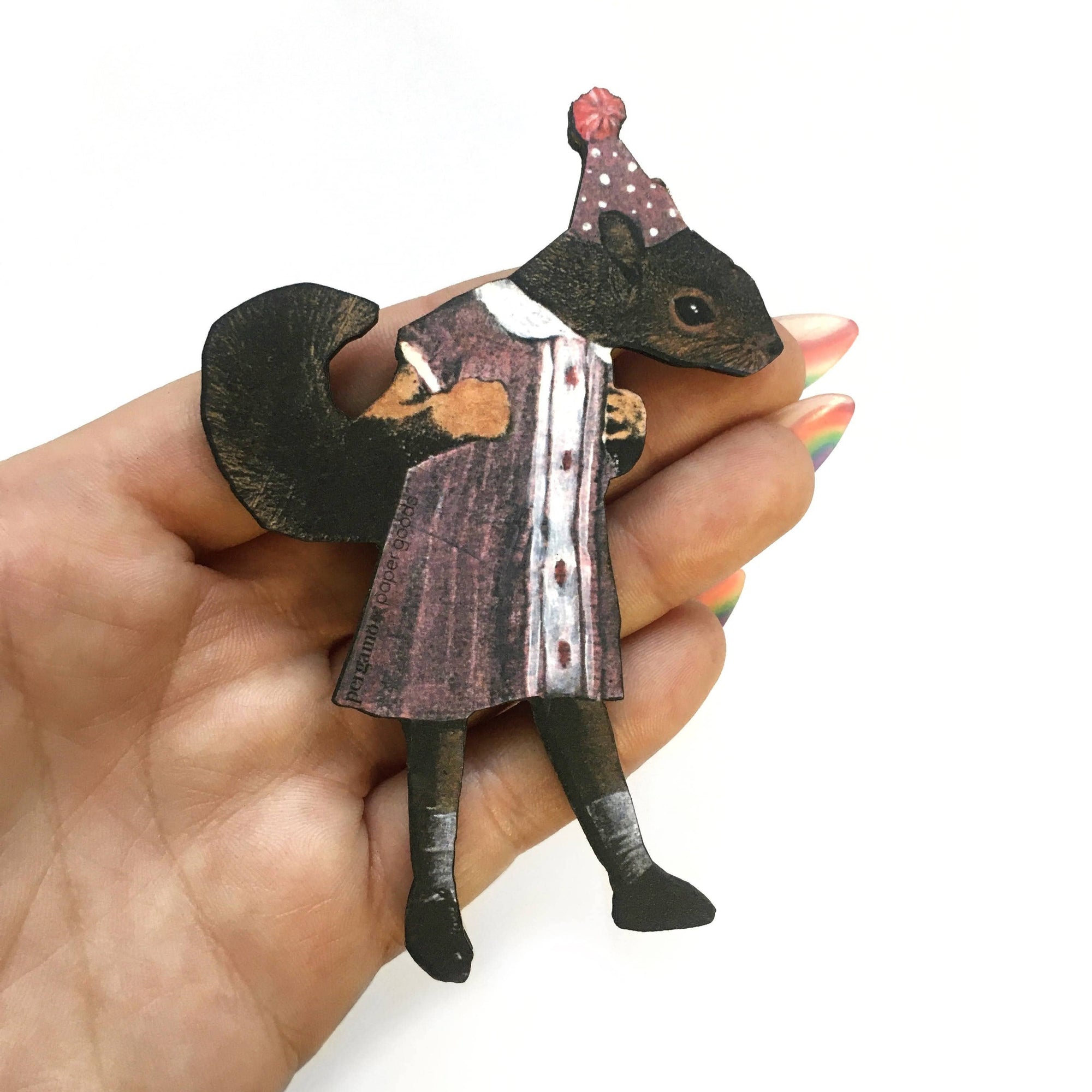 Hand holding a small figurine of a squirrel in a dress with a hat on a white background