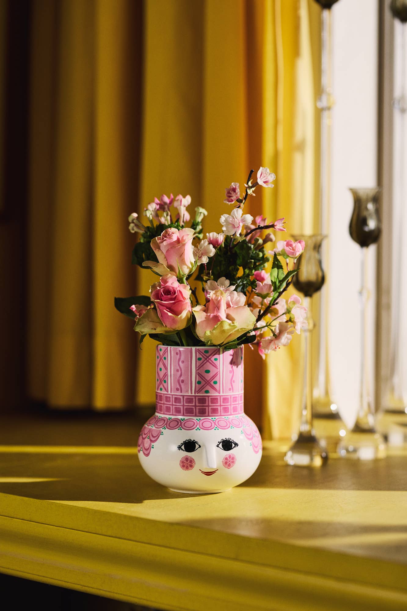 Decorative vase with a face and floral arrangement on a yellow surface