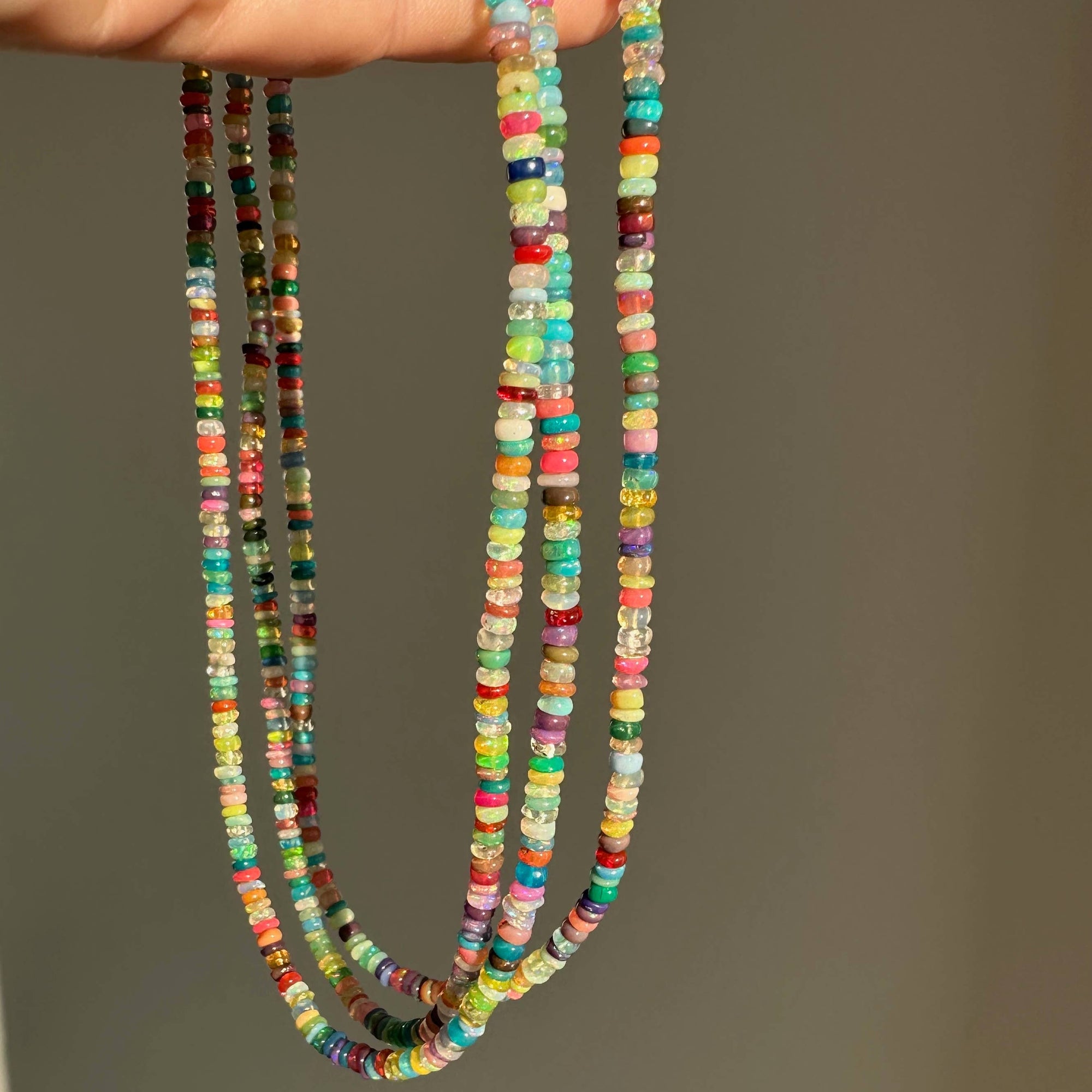 Colorful beaded necklaces held by a hand against a neutral background