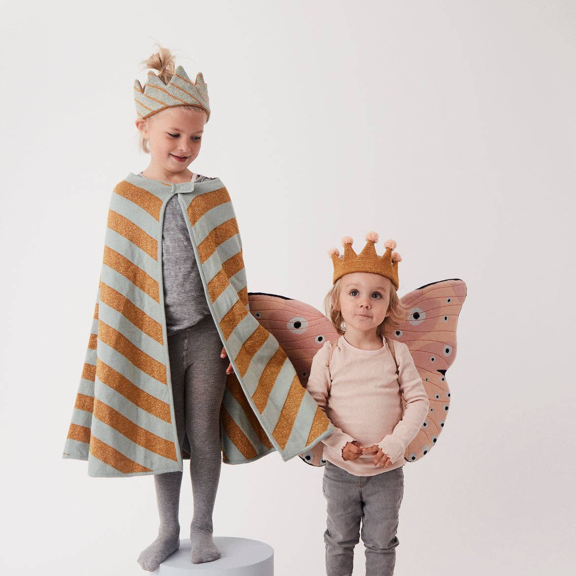 Two children in costume on stands with a plain background