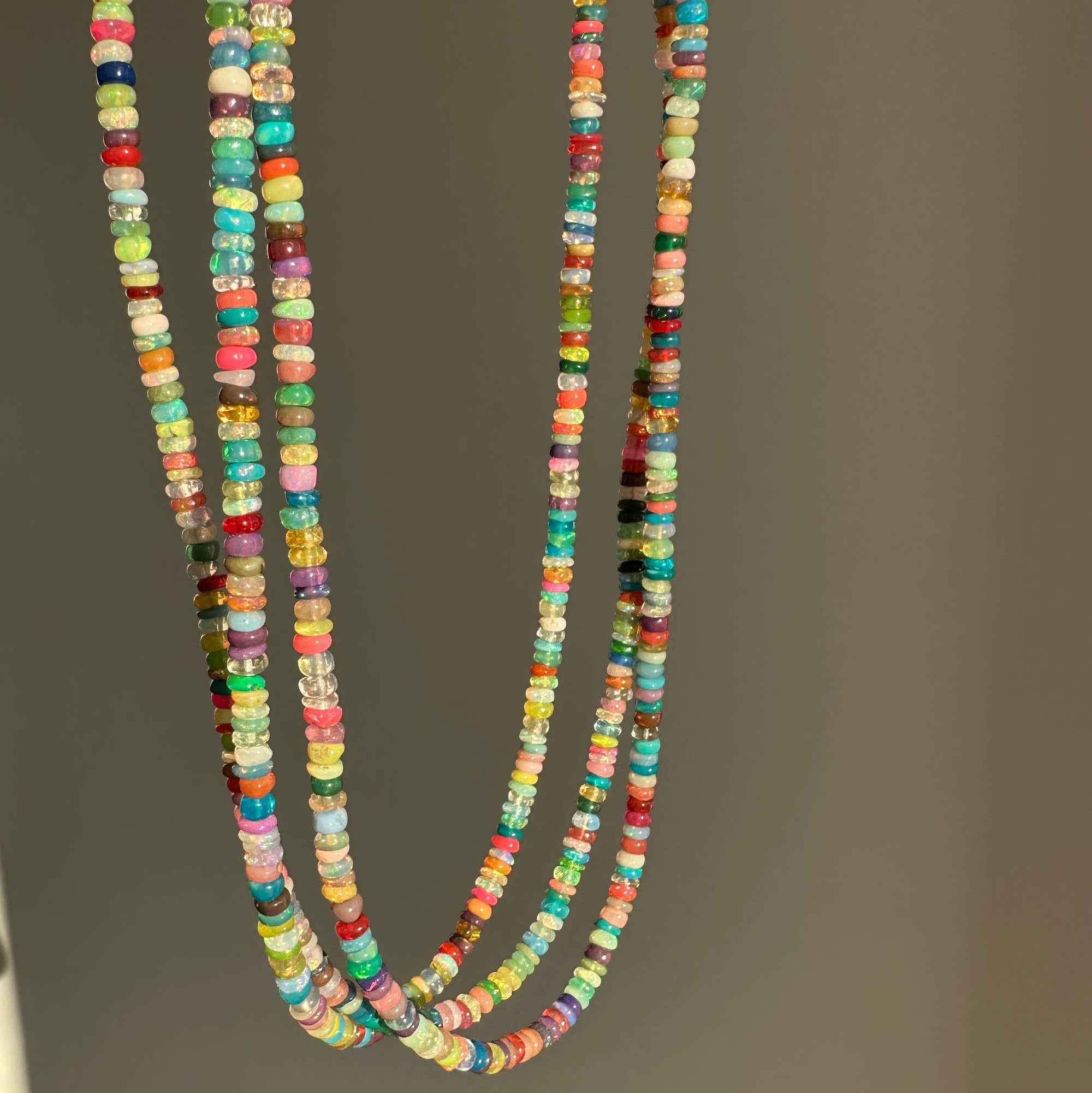 Colorful beaded necklace held by a hand against a neutral background