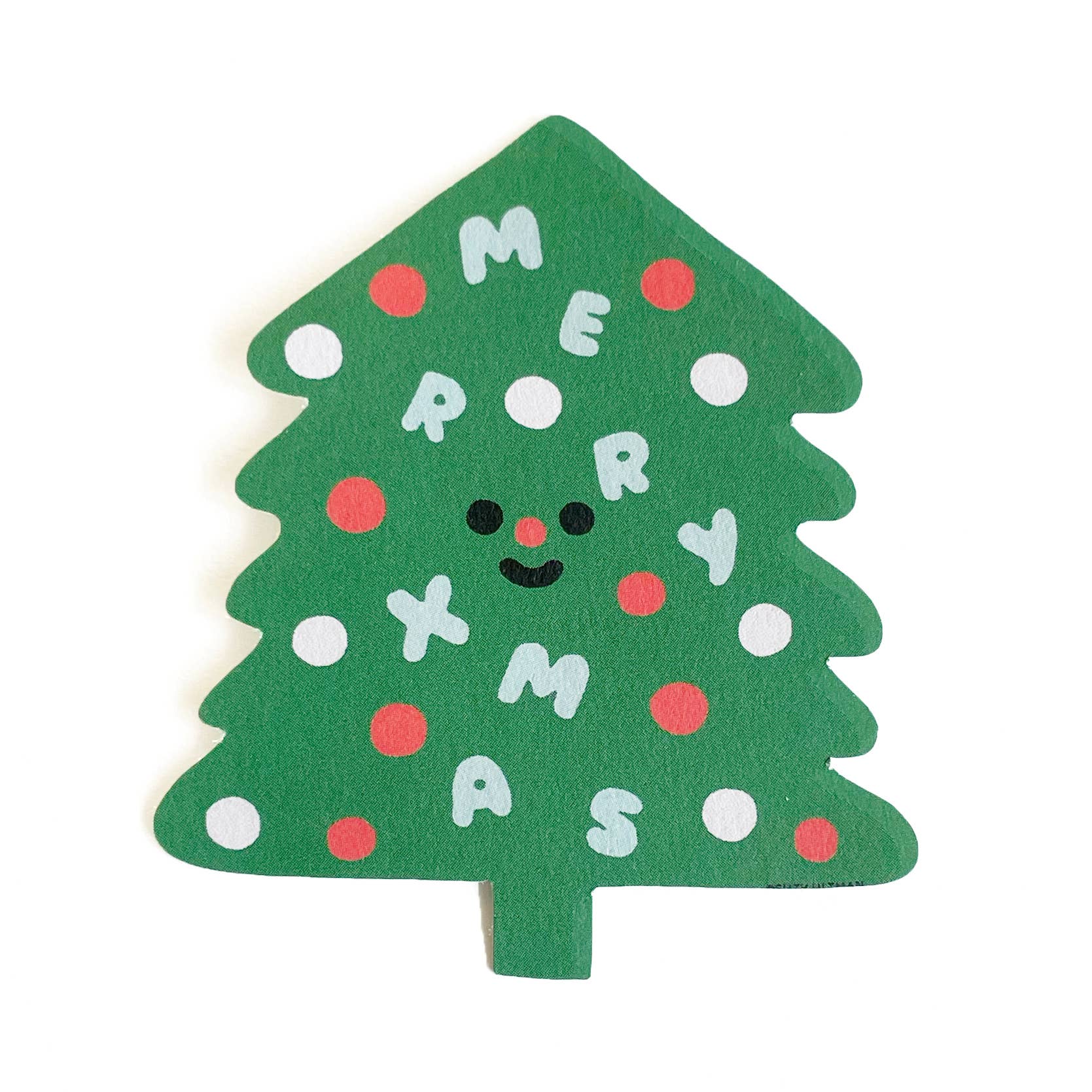 A diecut sticker in the shape of a Christmas tree with the phrase 'Merry Xmas' written on it, decorated with red and white dots and a smiling face.