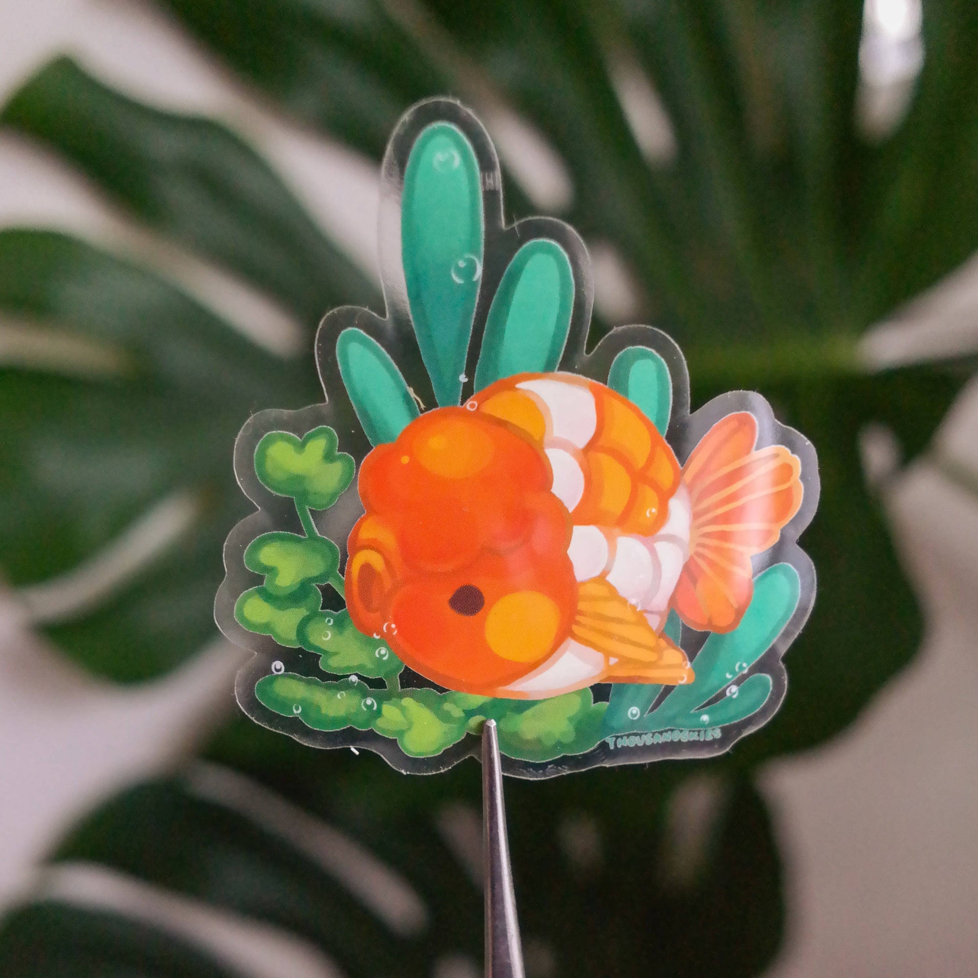 Decorative fish-shaped stake with green leaves against a blurred leafy background