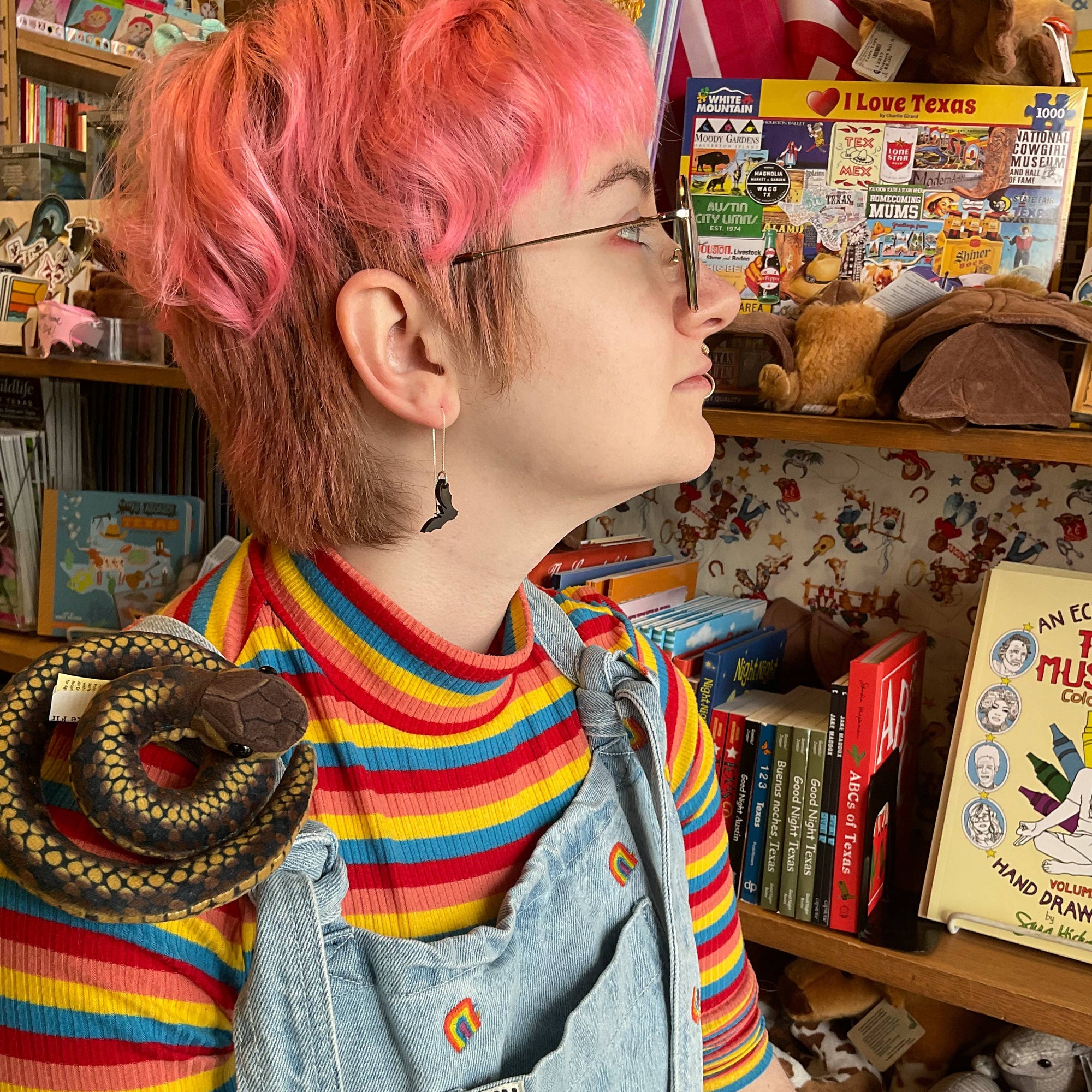 Person with pink hair and colorful outfit in a room filled with books and toys