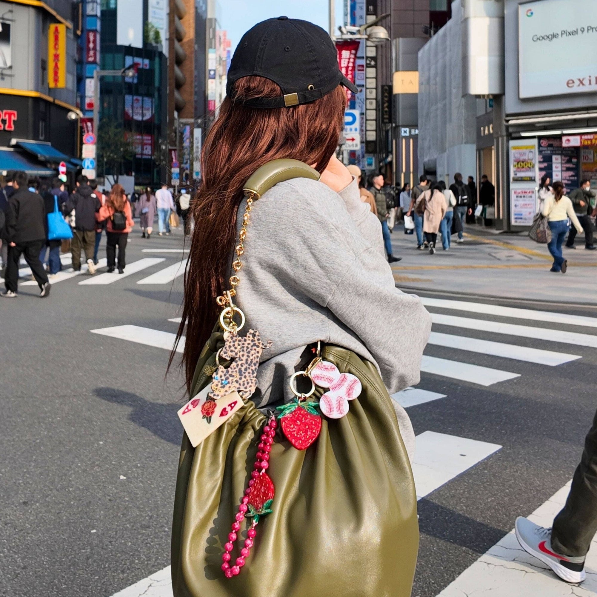 Person with a green bag adorned with colorful charms on a busy city street.