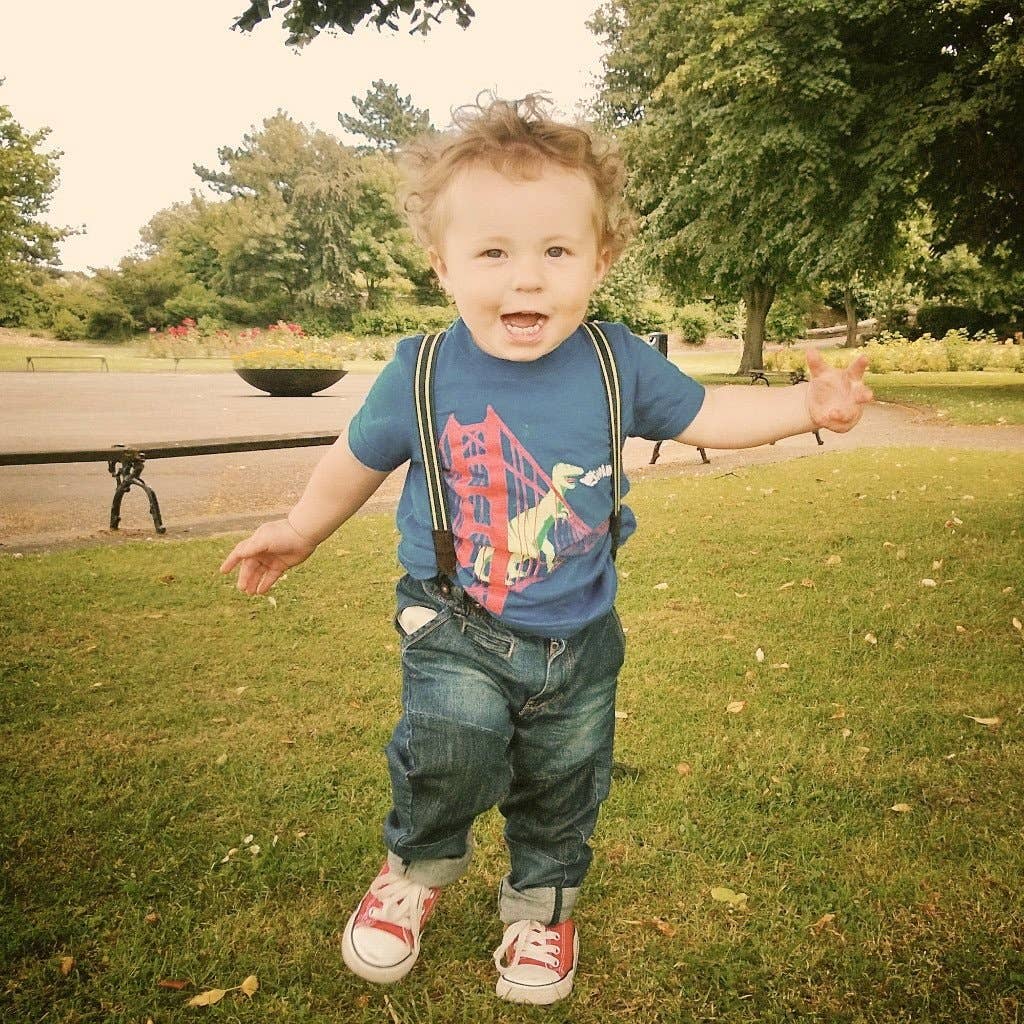 Child in a park wearing suspenders and a colorful shirt
