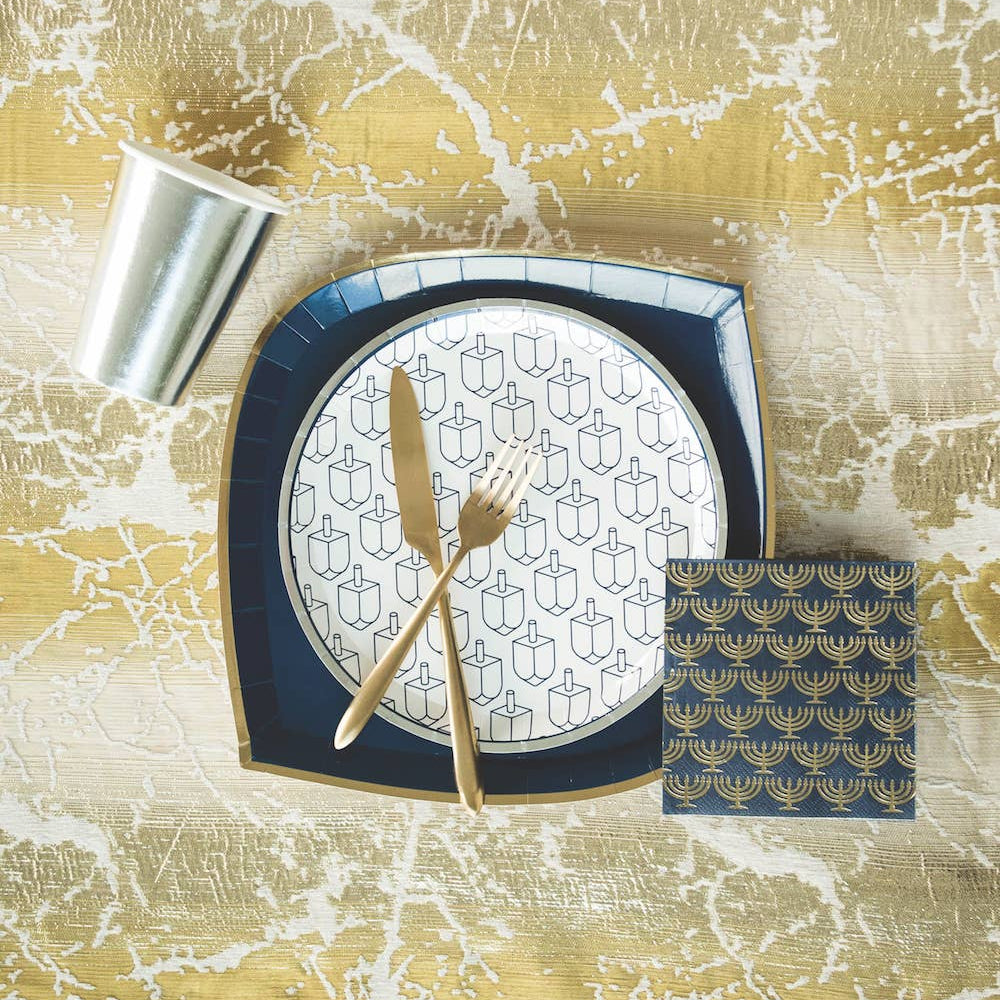 Dinner setting with a plate, knife, fork, and napkin on a textured gold surface.