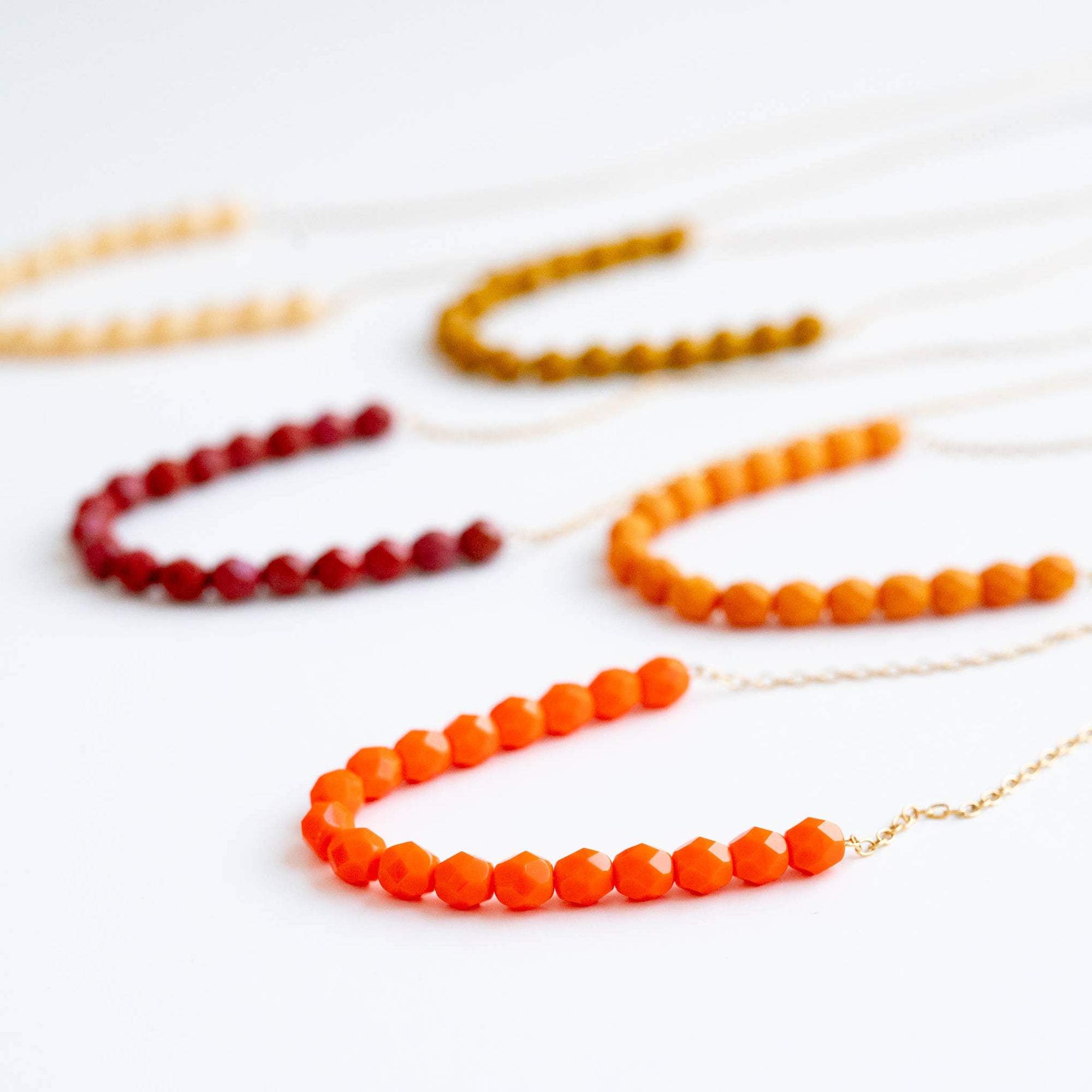 Set of beaded necklaces in red, orange, and gold on a white background