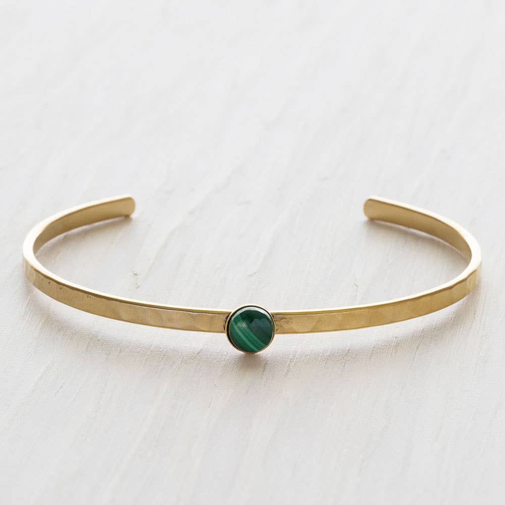 Gold bracelet with a green gemstone on a light background