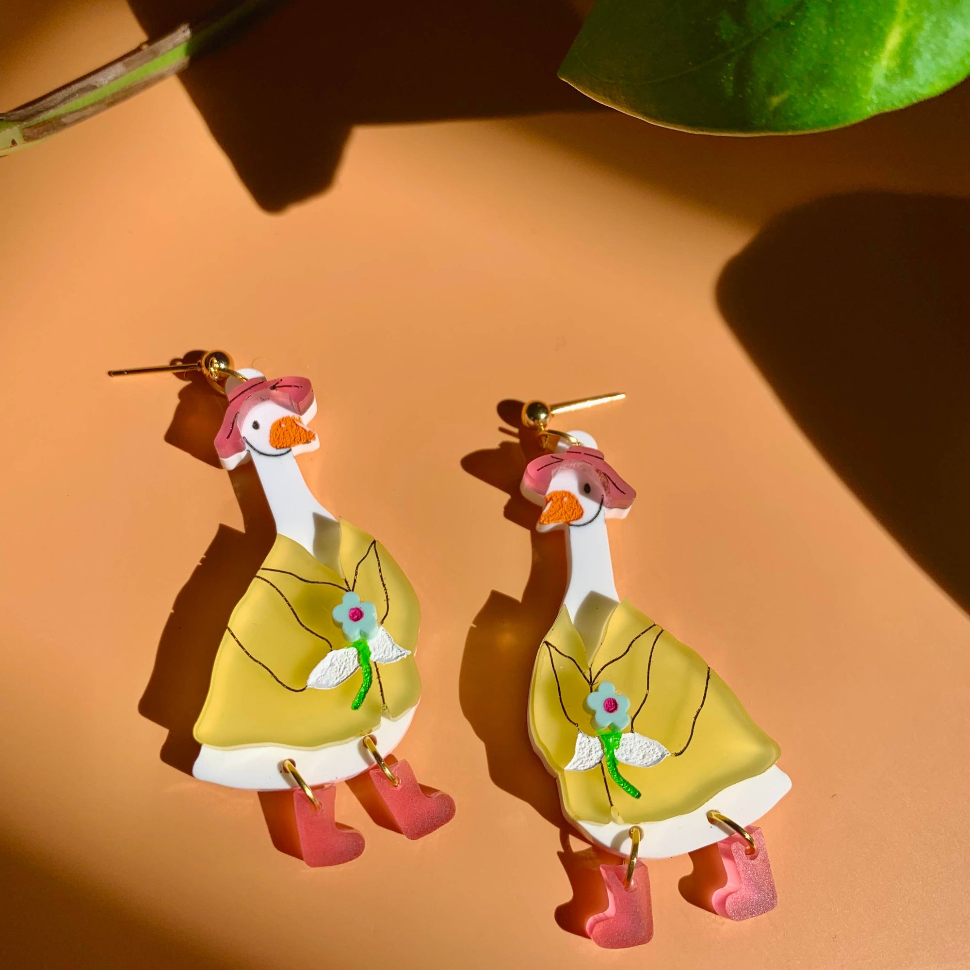 Pair of duck-shaped earrings on a brown background with a leaf