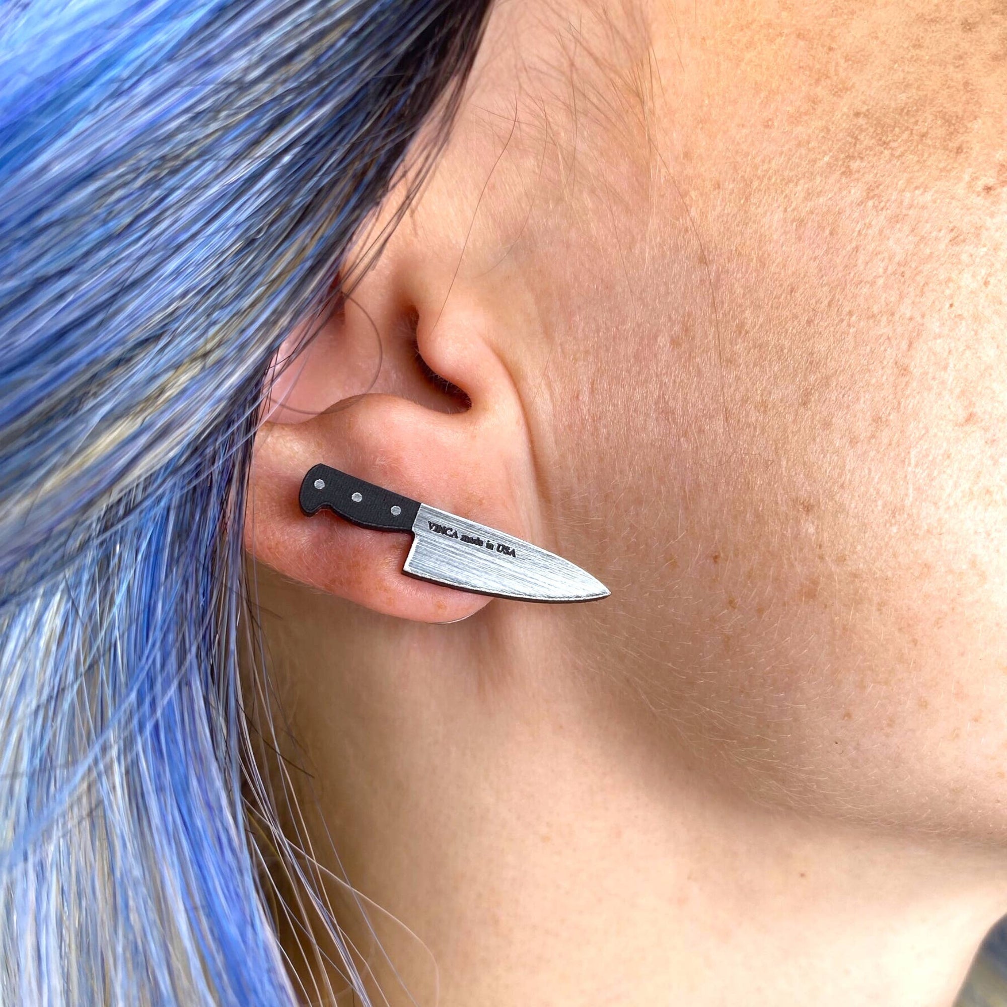 Knife-shaped earring worn by a person with blue hair.