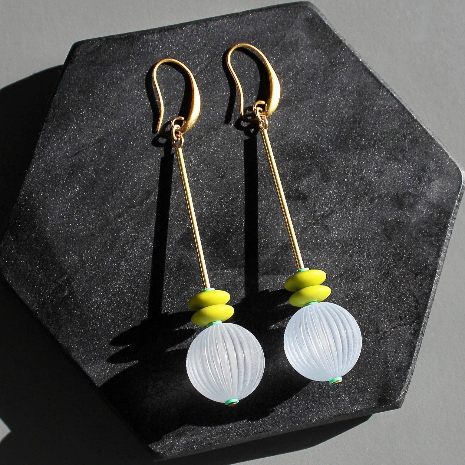 Gold earrings with white spherical beads on a dark gray hexagonal stand