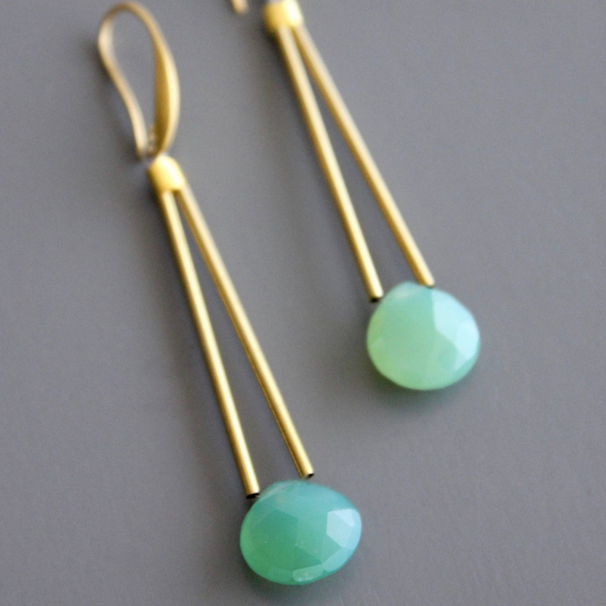 Gold earrings with green beads on a gray background
