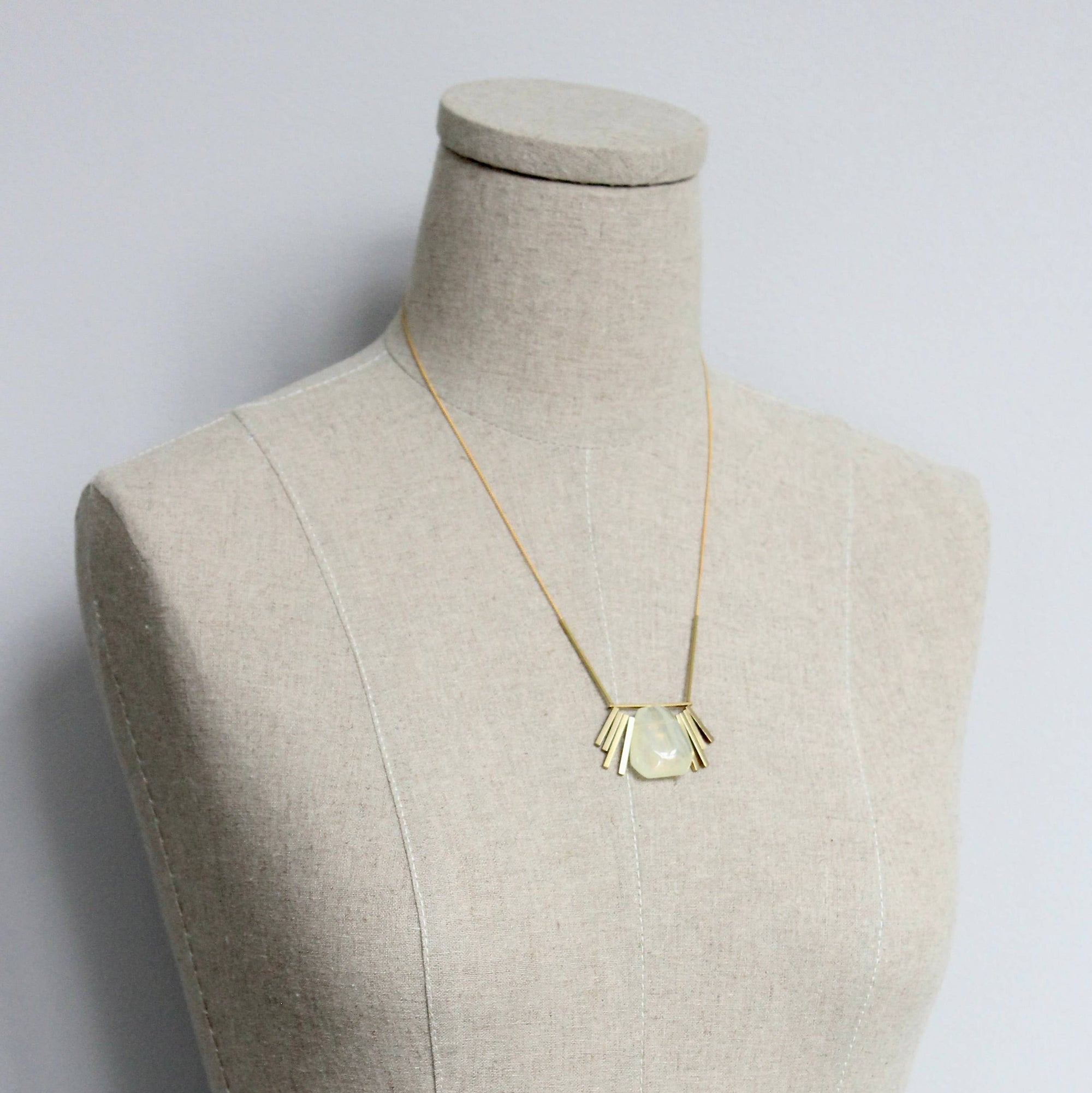 Gold necklace with a pendant on a mannequin bust against a plain background