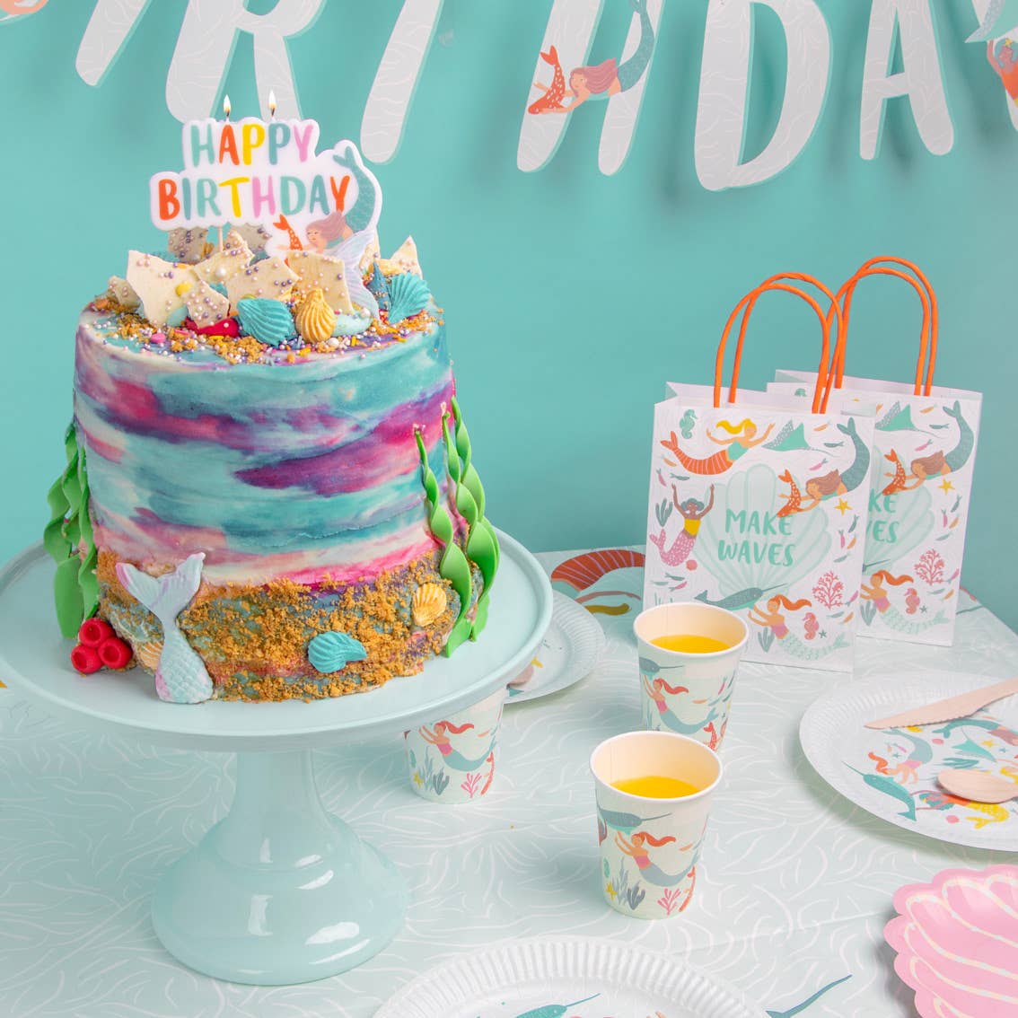 Birthday cake with mermaid theme decorations on a table with matching party supplies.