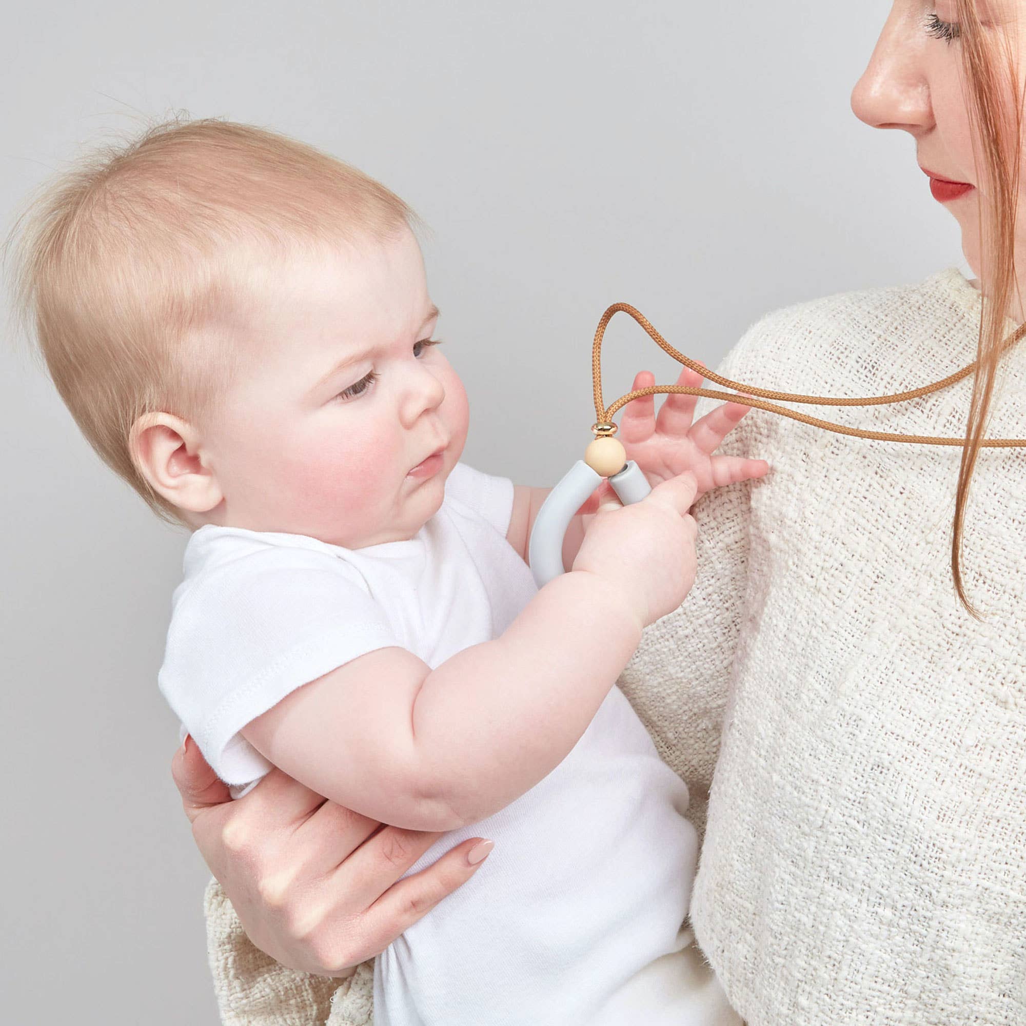 Woman holding a baby and showing a necklace.