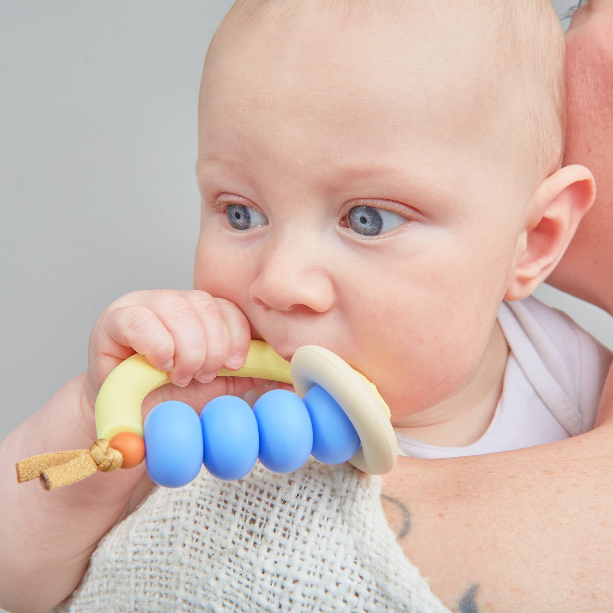 Baby holding a blue and yellow teething ring with a neutral background