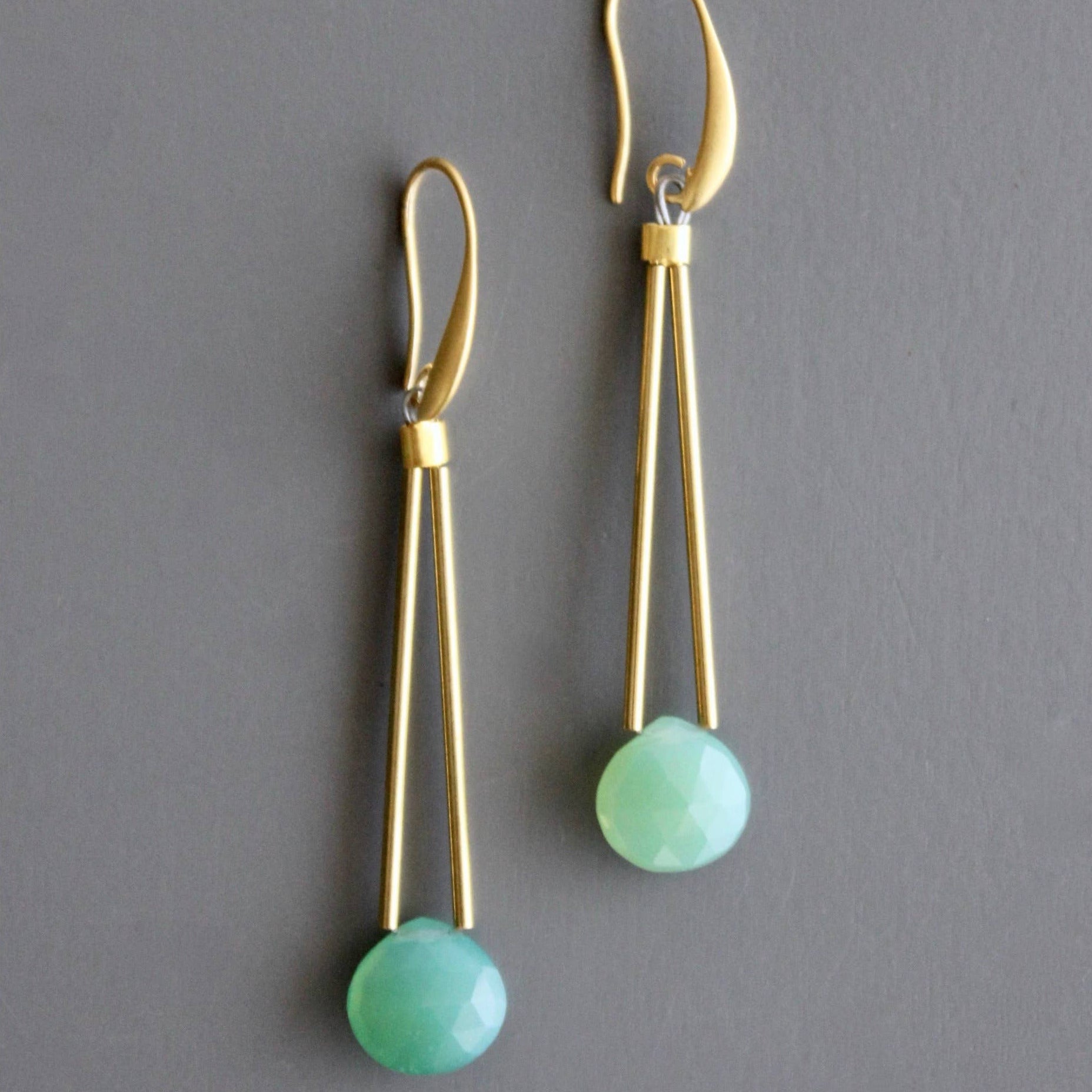 Gold earrings with green beads on a gray background