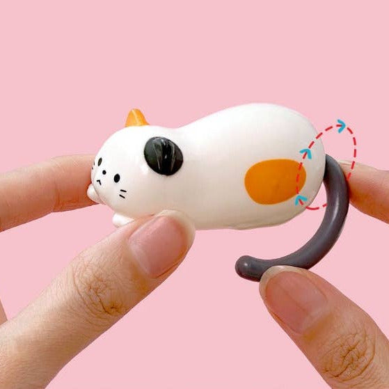 White cat-shaped figure with orange spots held between fingers against a pink background