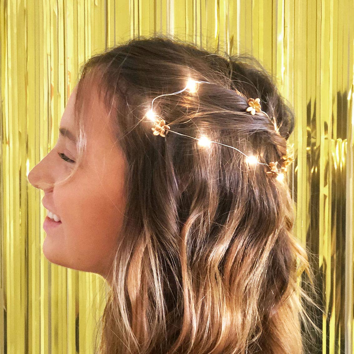 Woman with fairy lights in her hair against a gold tinsel background