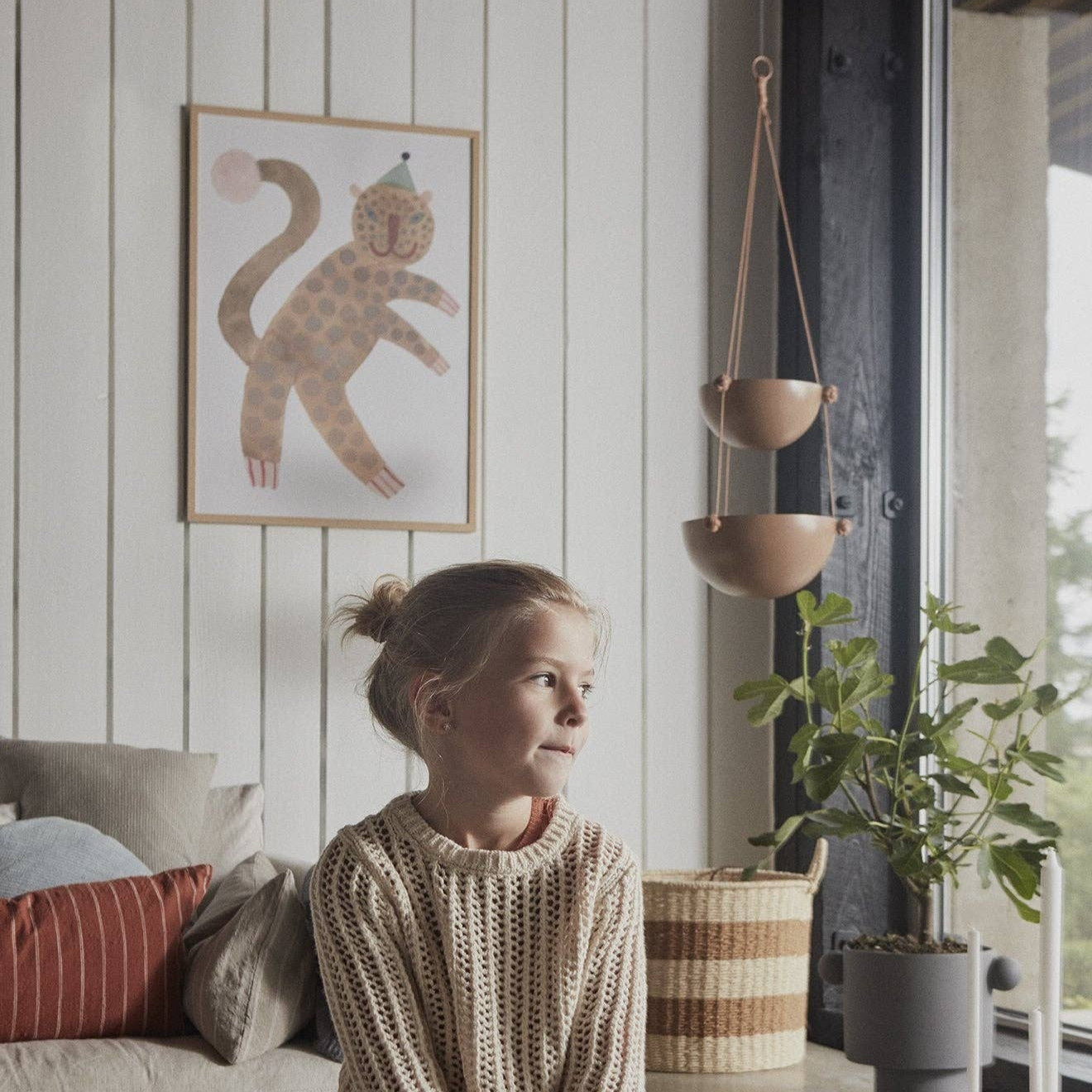 Woman sitting on a stool in a cozy room with plants and decor.