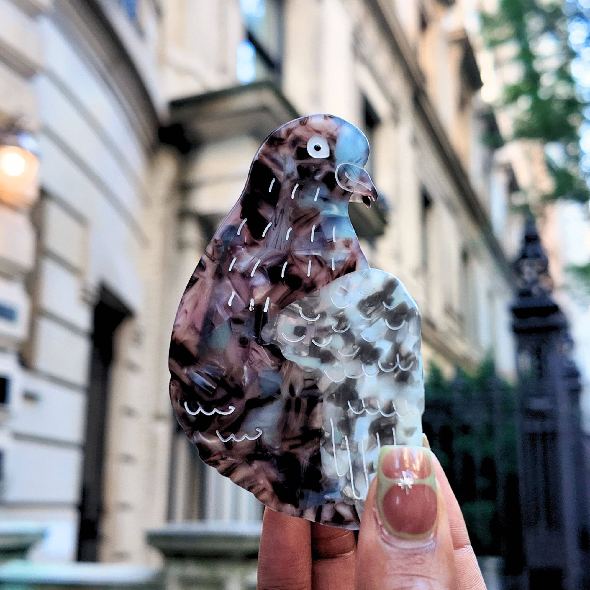 Hand holding a colorful pigeon-shaped object with a blurred cityscape background