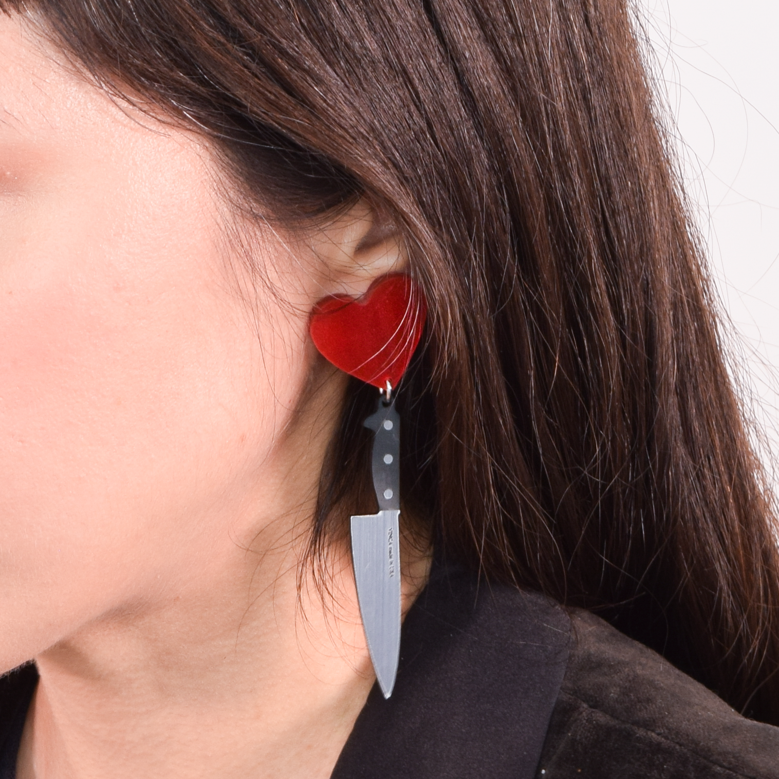 Red heart-shaped earring with a knife blade worn by a person.