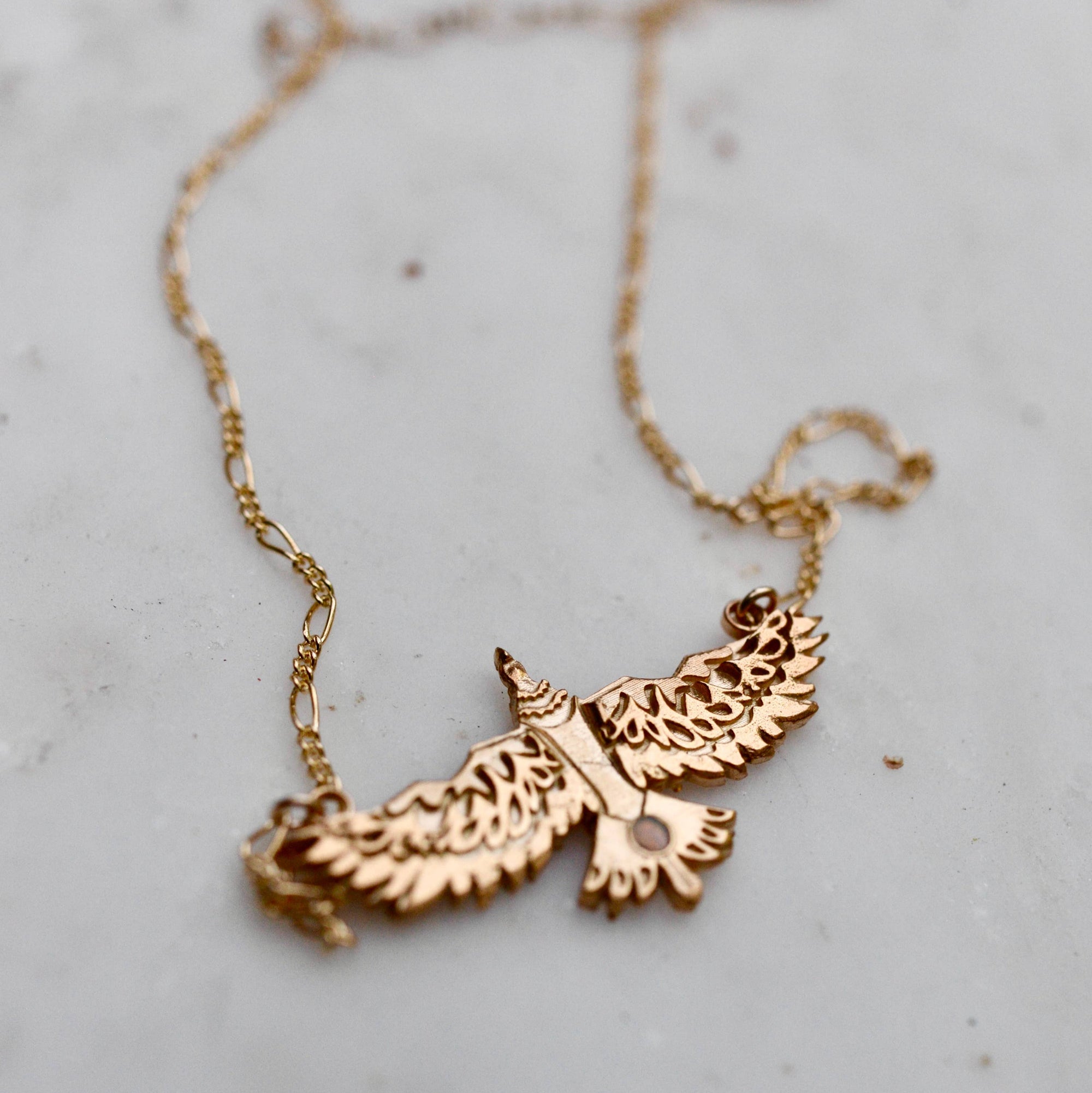 Gold necklace with an eagle pendant on a light gray surface