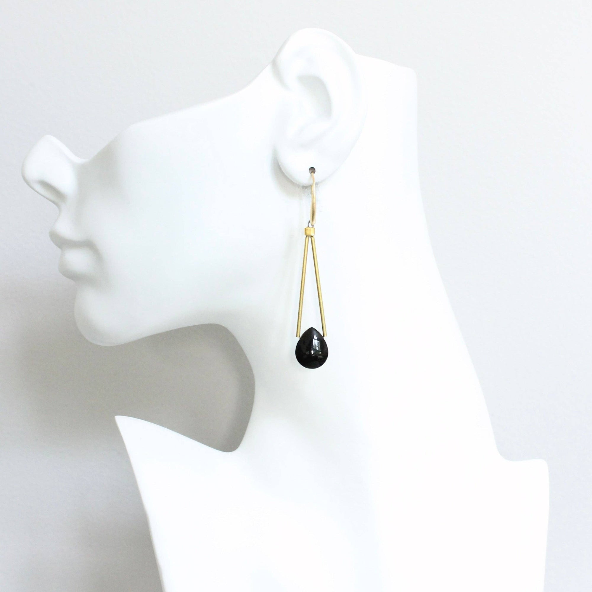 Black teardrop earring on a white mannequin ear against a white background