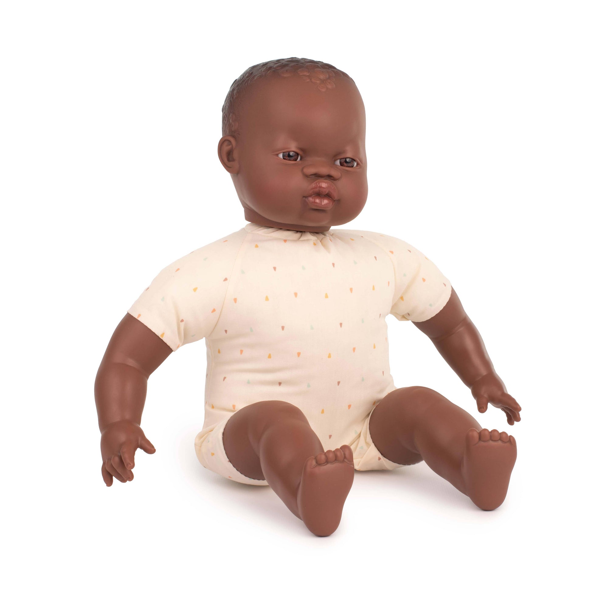 Doll of a baby with dark skin and brown hair wearing a white onesie on a white background