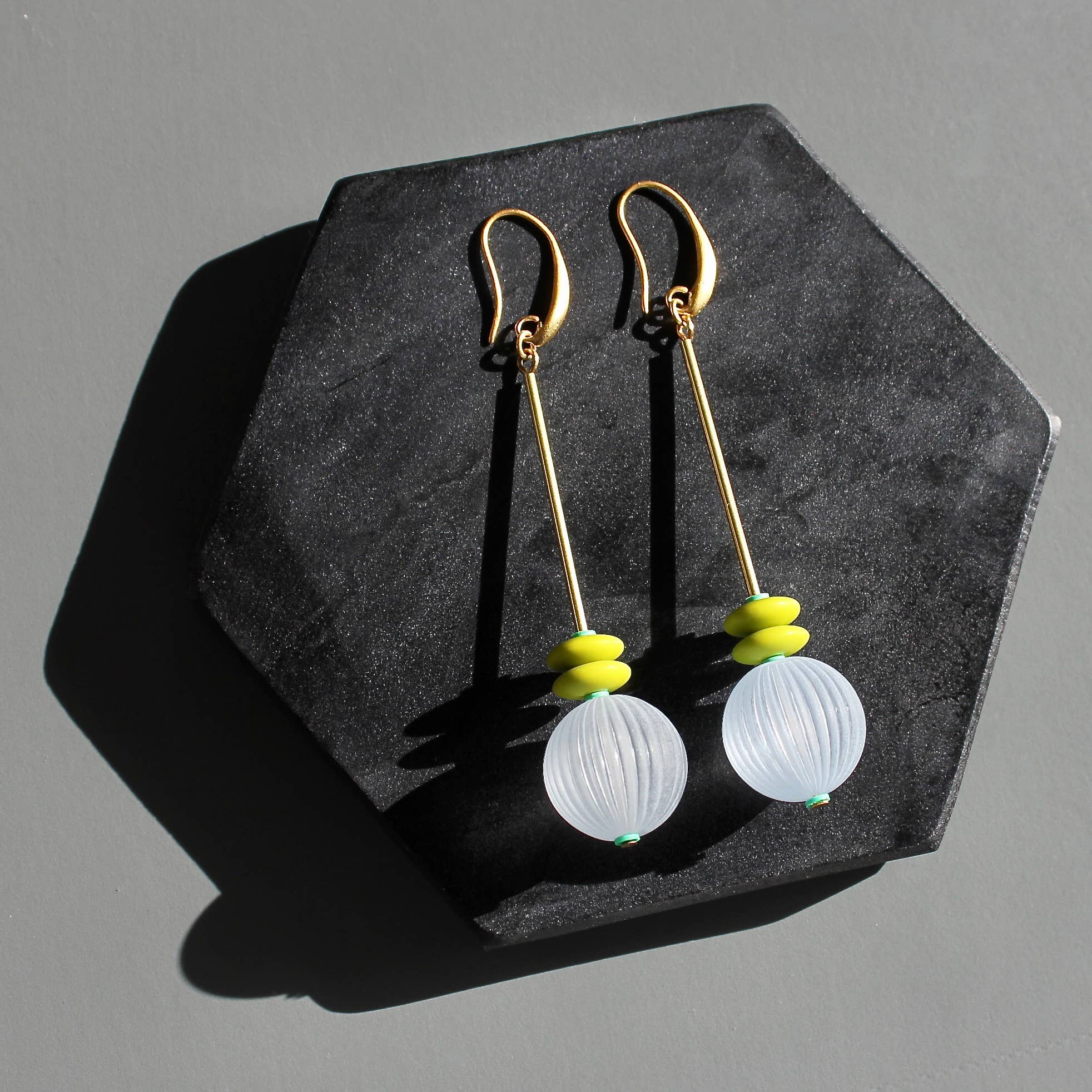 Pair of earrings with gold hooks, white spherical beads, and green accents on a dark stone surface.