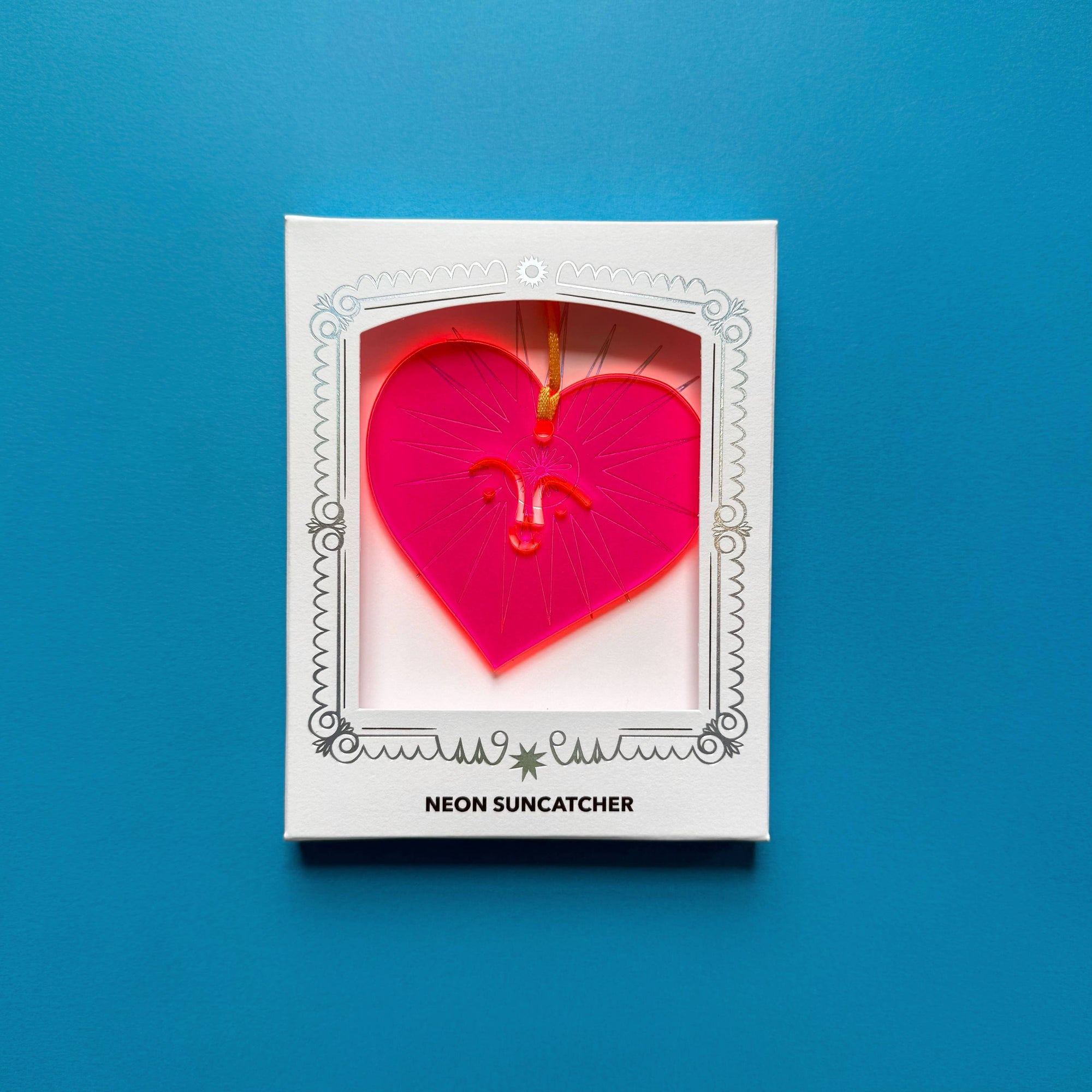 Neon pink heart-shaped suncatcher in a white box on a blue background
