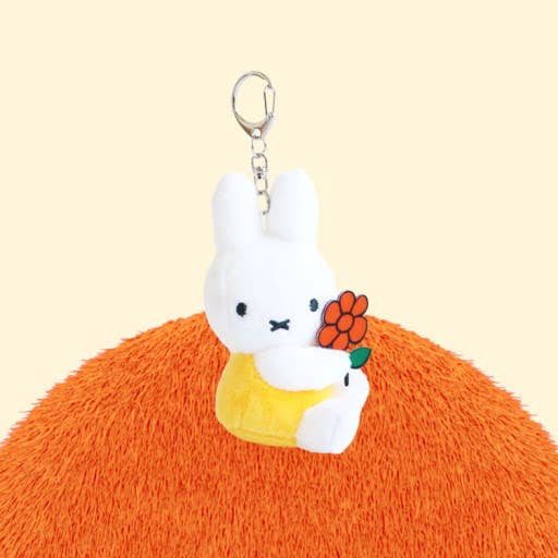 Plush keychain of a white rabbit character with a yellow dress on an orange surface.