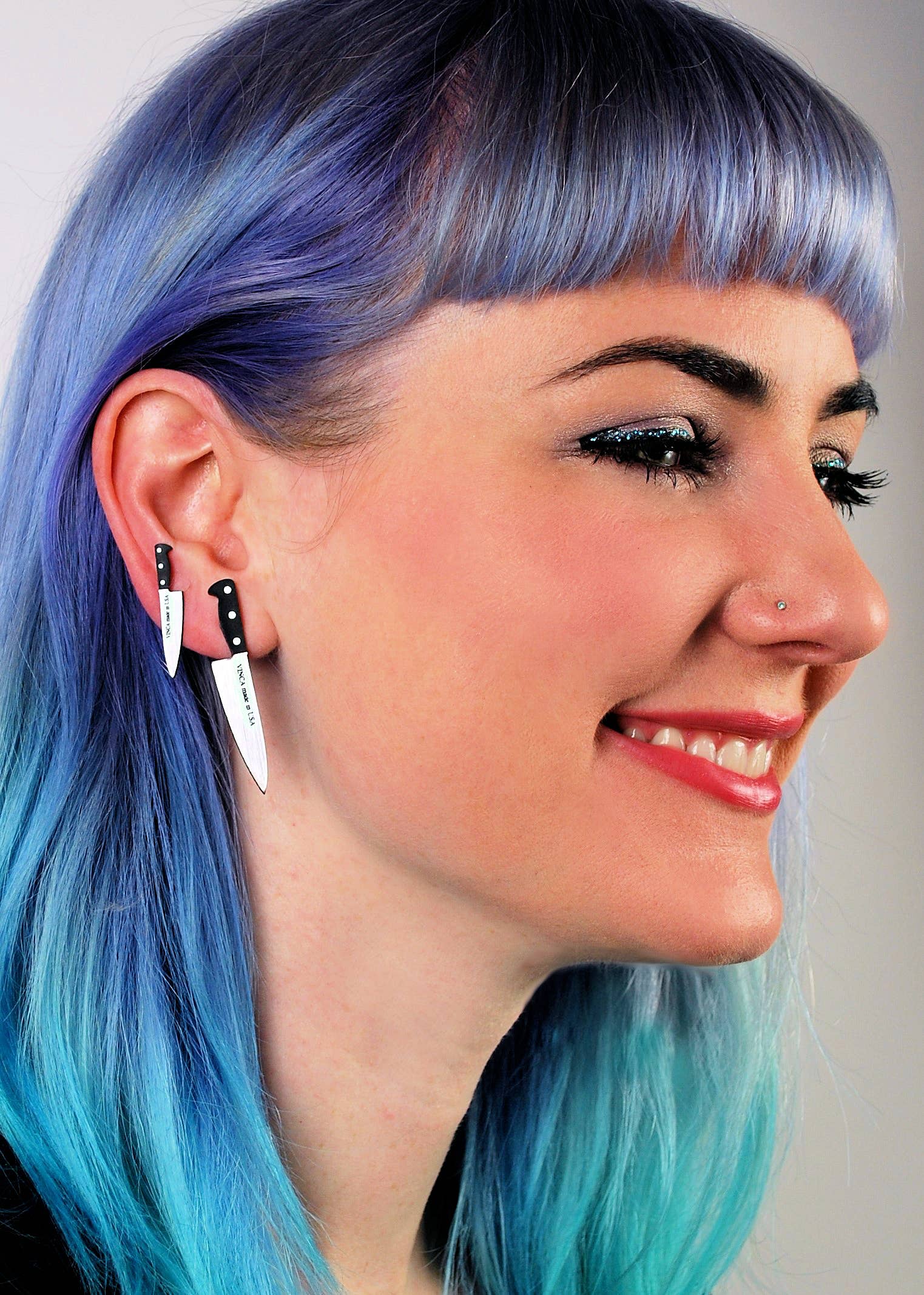 Person with blue hair wearing black and white knife-shaped earrings.
