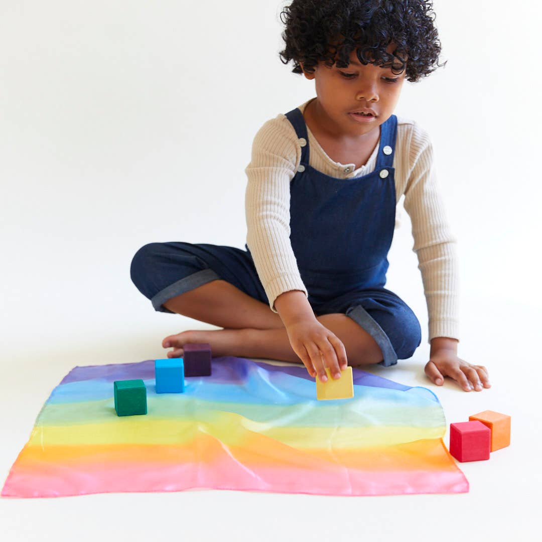 Child playing with colorful blocks on a rainbow mat