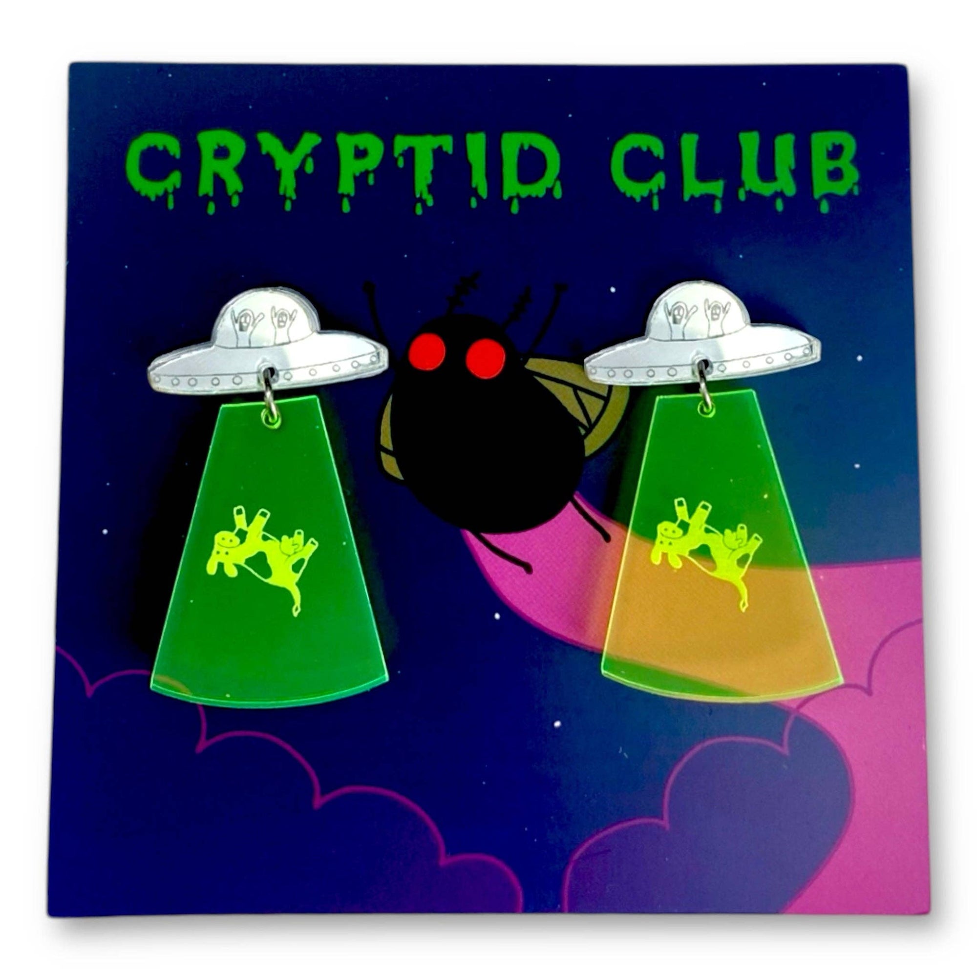 Pair of earrings with UFO and alien design on a 'Cryptid Club' card.
