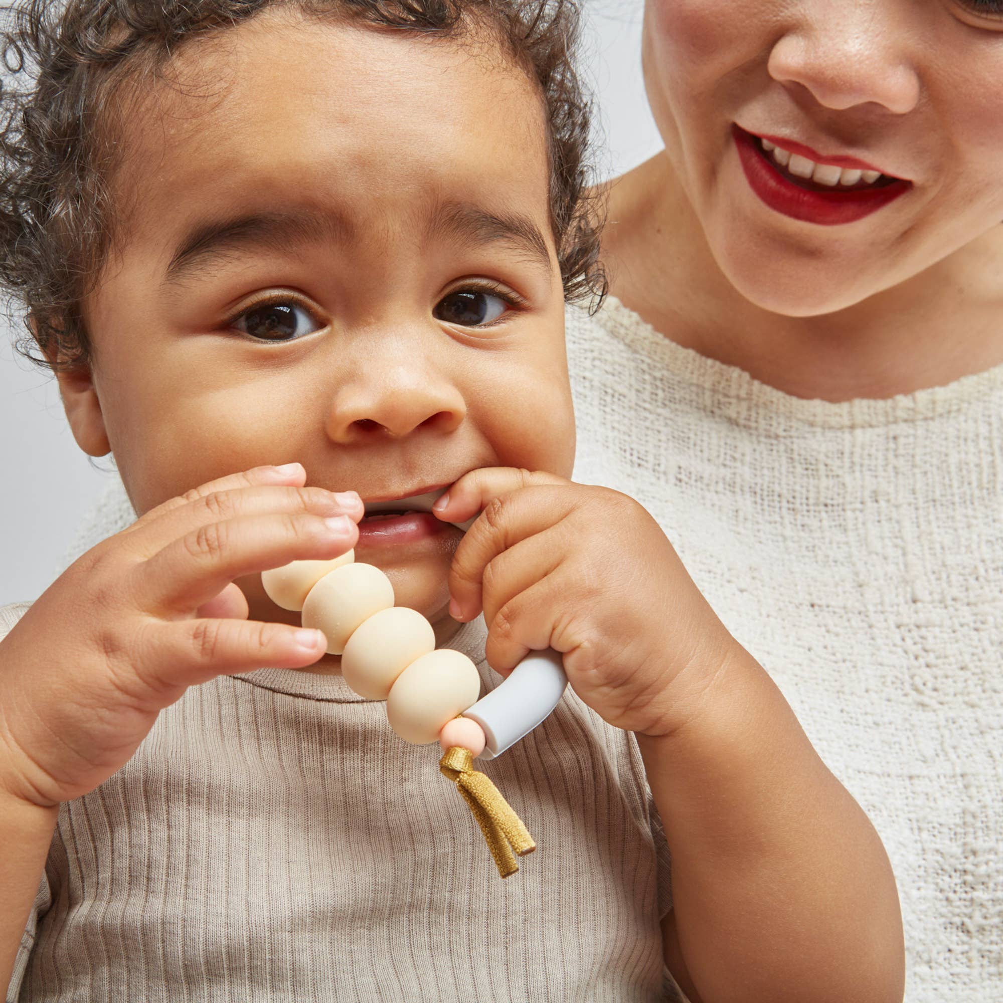 Baby holding a teething toy with a blurred person in the background