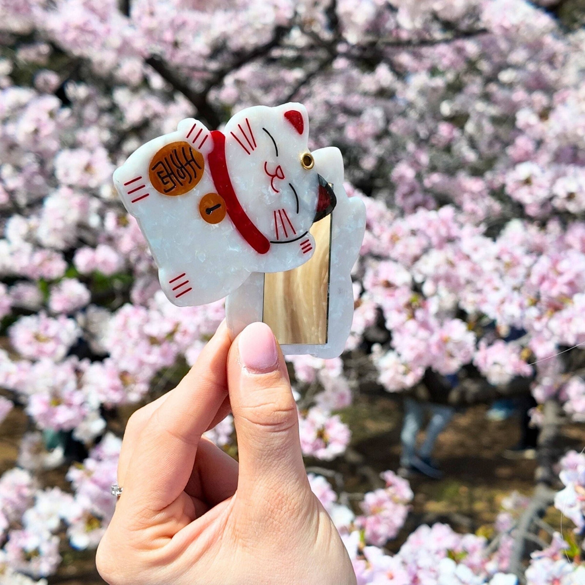 Hand holding a small cat-shaped object with cherry blossoms in the background