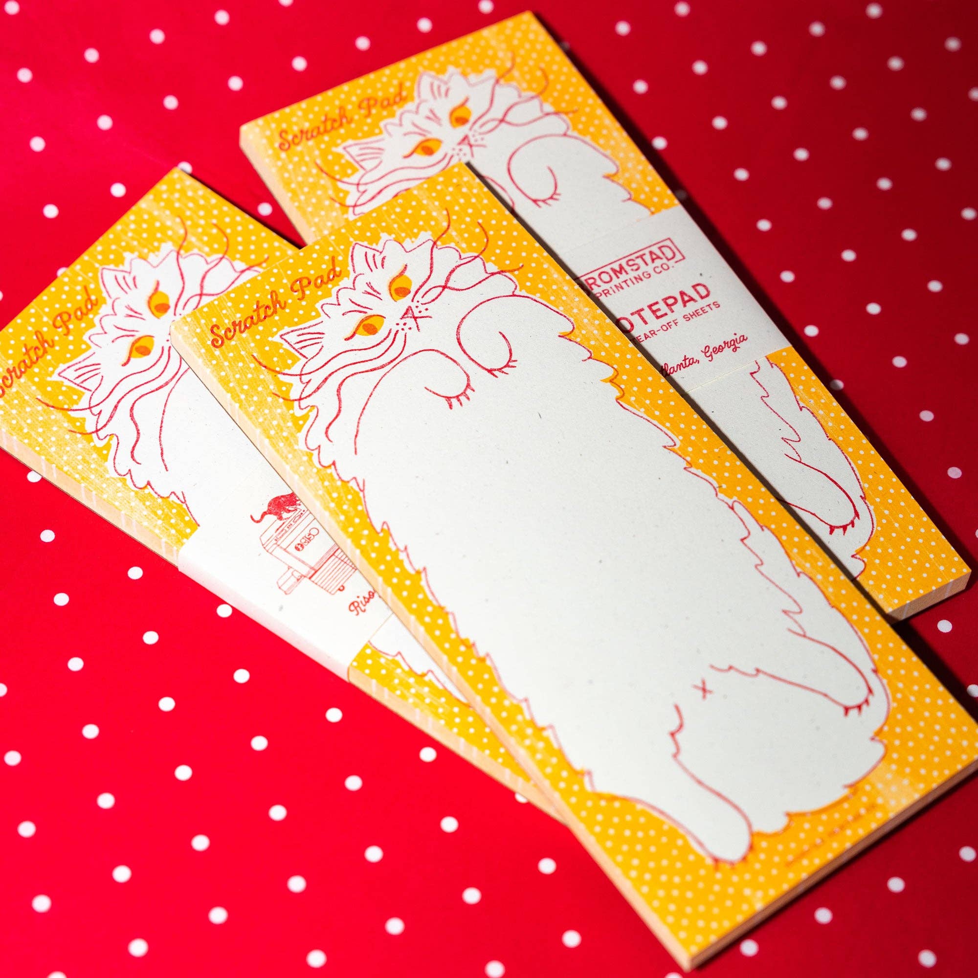 Three small pads with cat illustrations on a red polka dot background