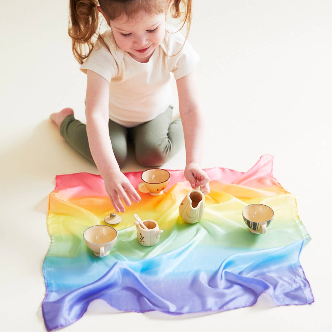 Child playing with small containers on a colorful rainbow blanket