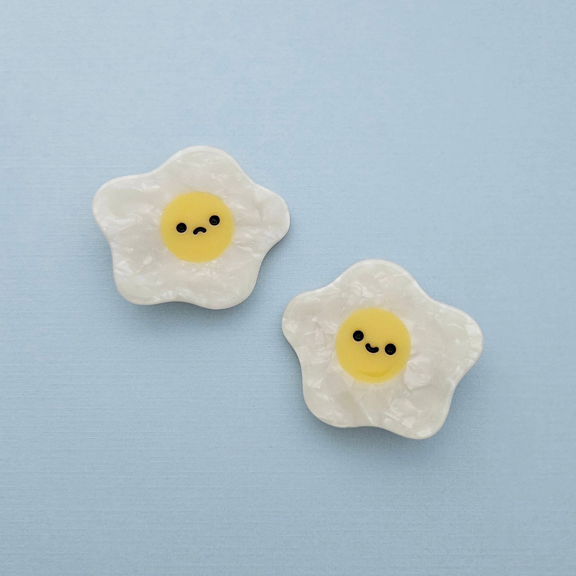 Two cute emoji-style fried eggs with faces on a light blue background