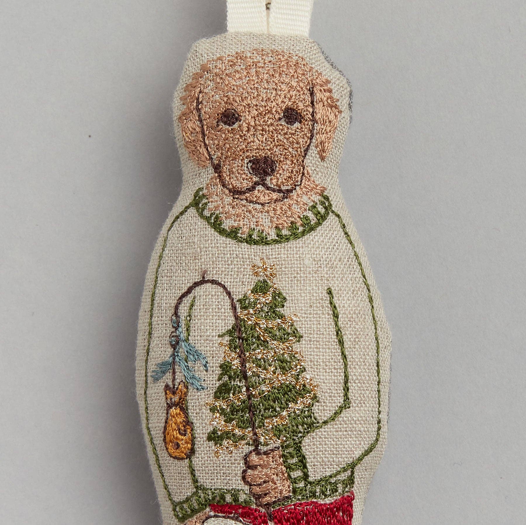 Decorative dog ornament with a sweater holding a Christmas tree and other items on a gray background
