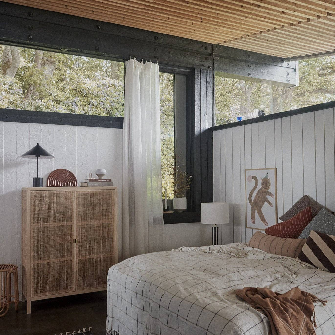 Modern bedroom with wooden ceiling, large windows, and a bed with plaid blanket.
