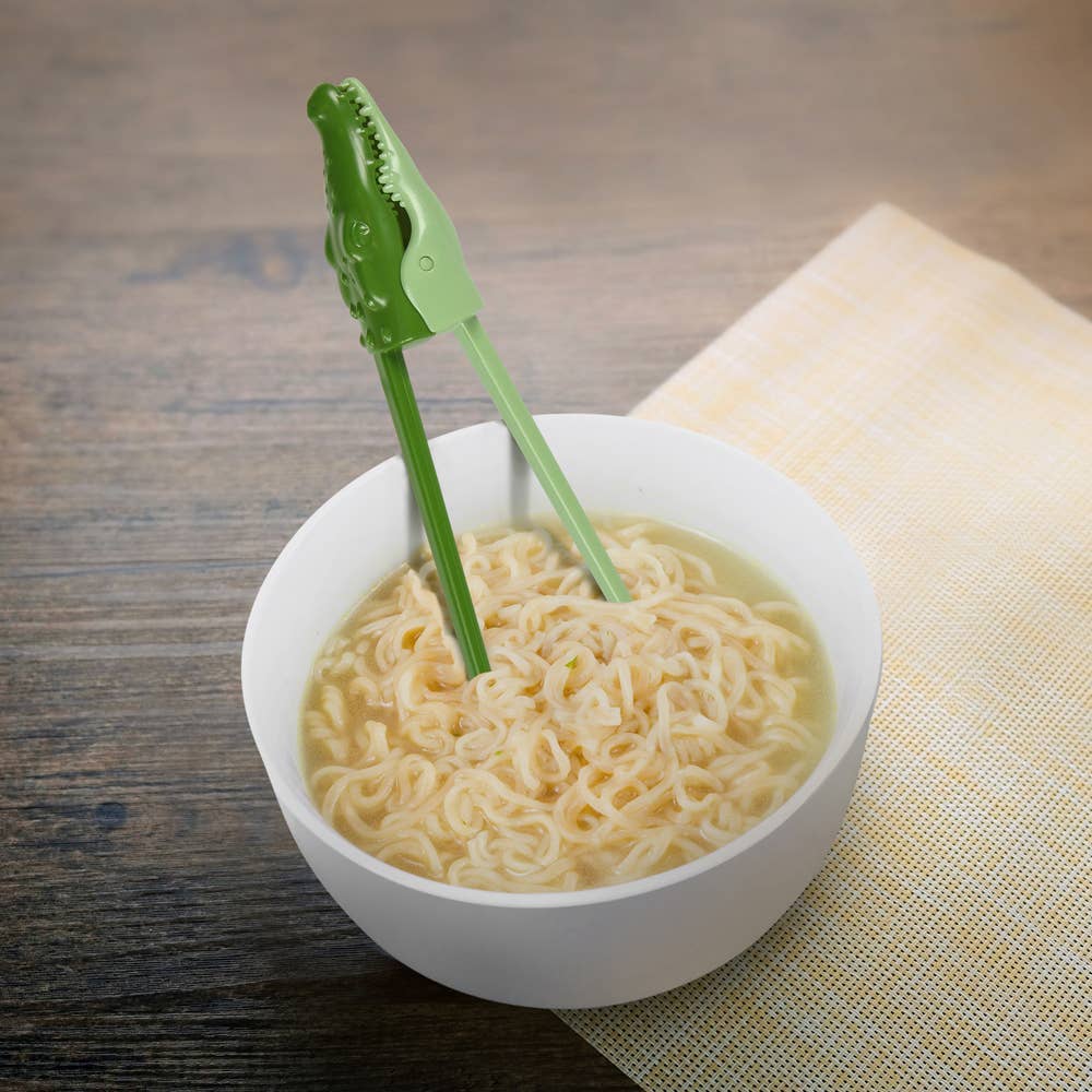 Green tongs in a bowl of ramen on a wooden surface