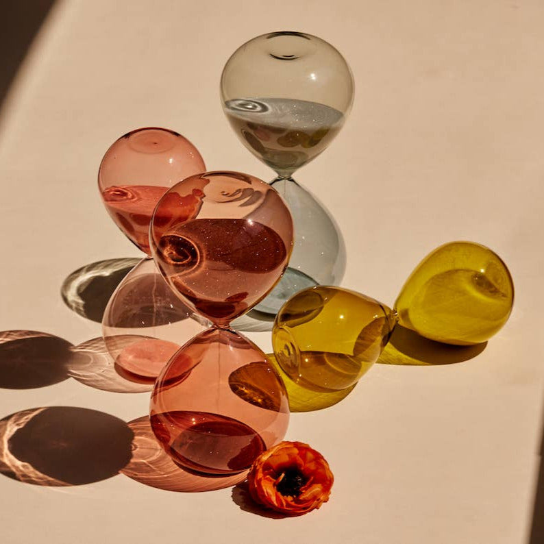 Colorful glass hourglasses on a reflective surface with a flower.