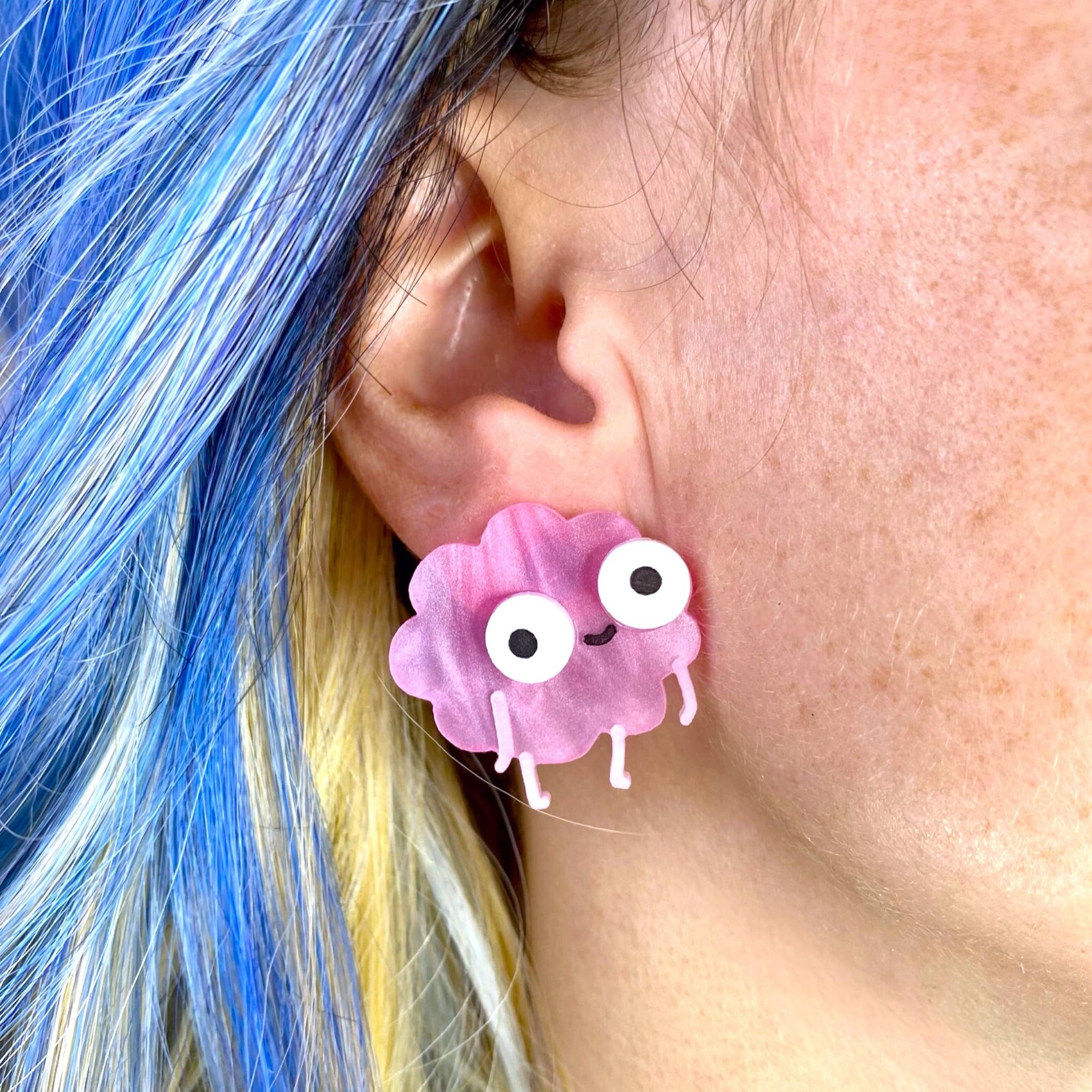 Person wearing a pink cartoonish earrings with googly eyes and a smile.