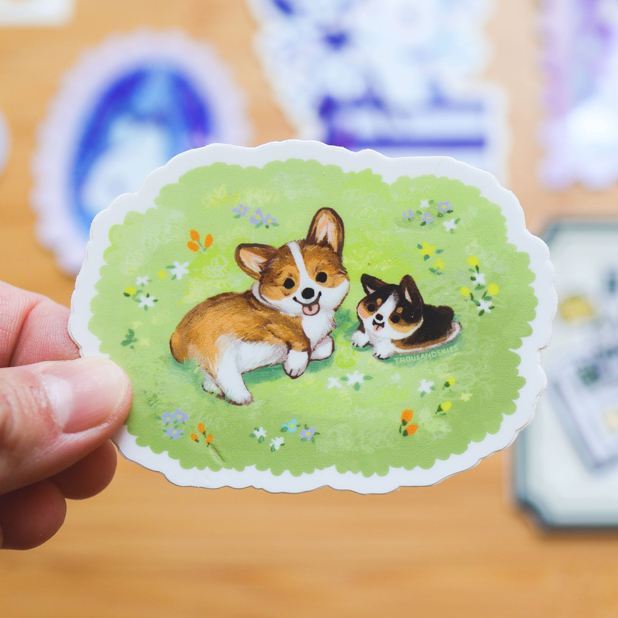 Sticker with two corgis on a green background held by a hand.