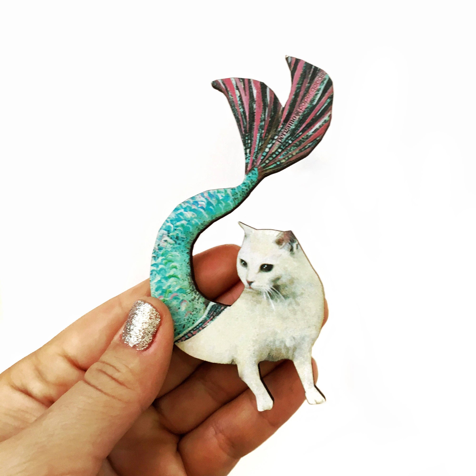 Cat figurine with a colorful mermaid tail held by a hand on a white background