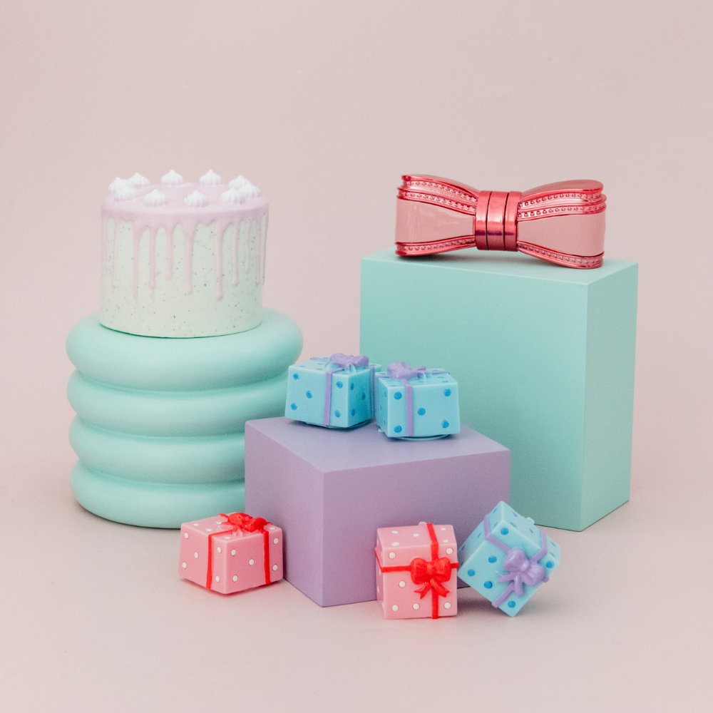 Pastel-colored cake and gift boxes with decorative ribbons on a light pink background