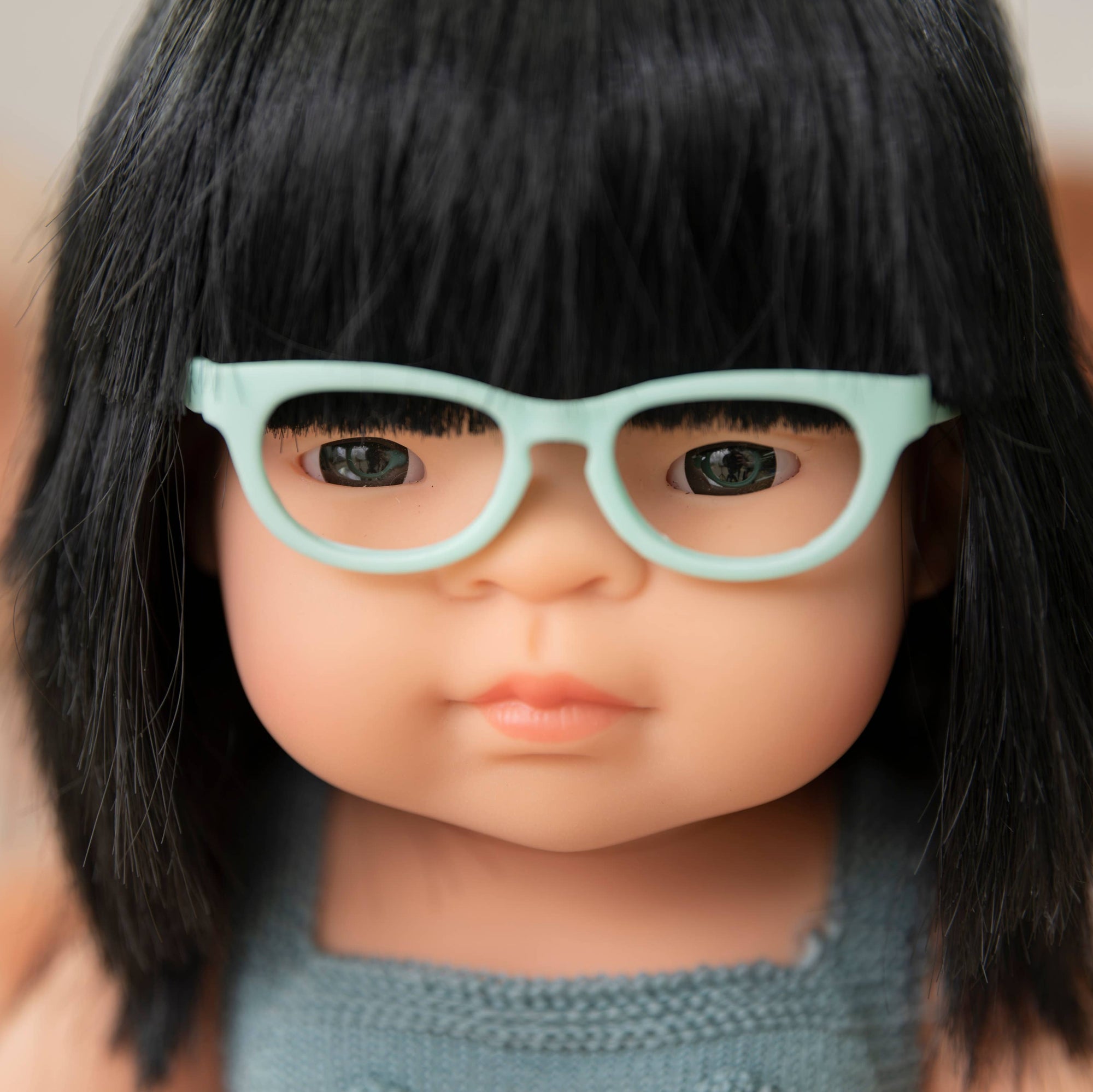 Close-up of a doll with black hair and light blue glasses against a blurred background